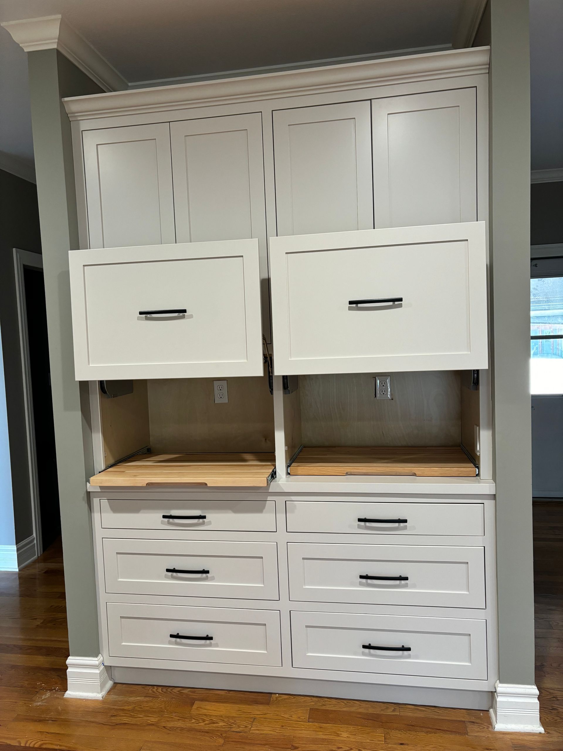 White built-in cabinetry with drawers and open compartments against a gray wall, on a wood floor.