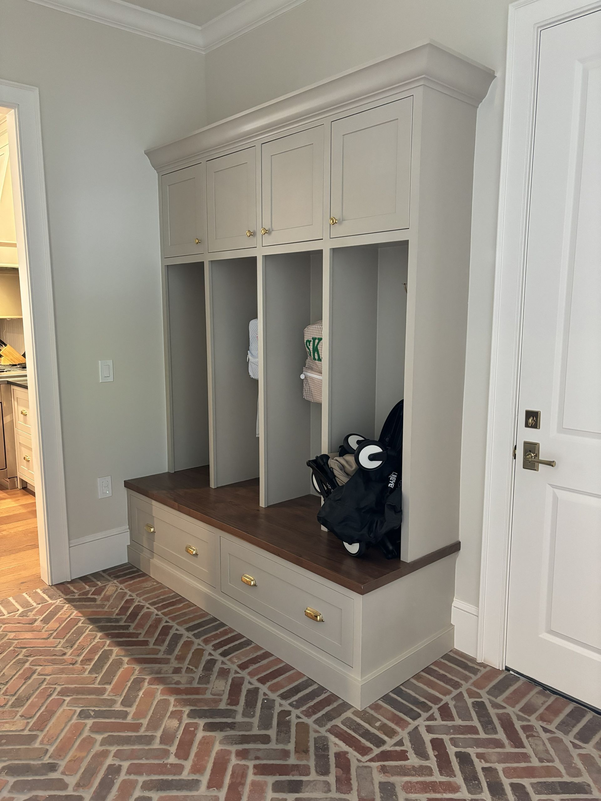 A mudroom with a built-in bench, storage cabinets, and brick floor.