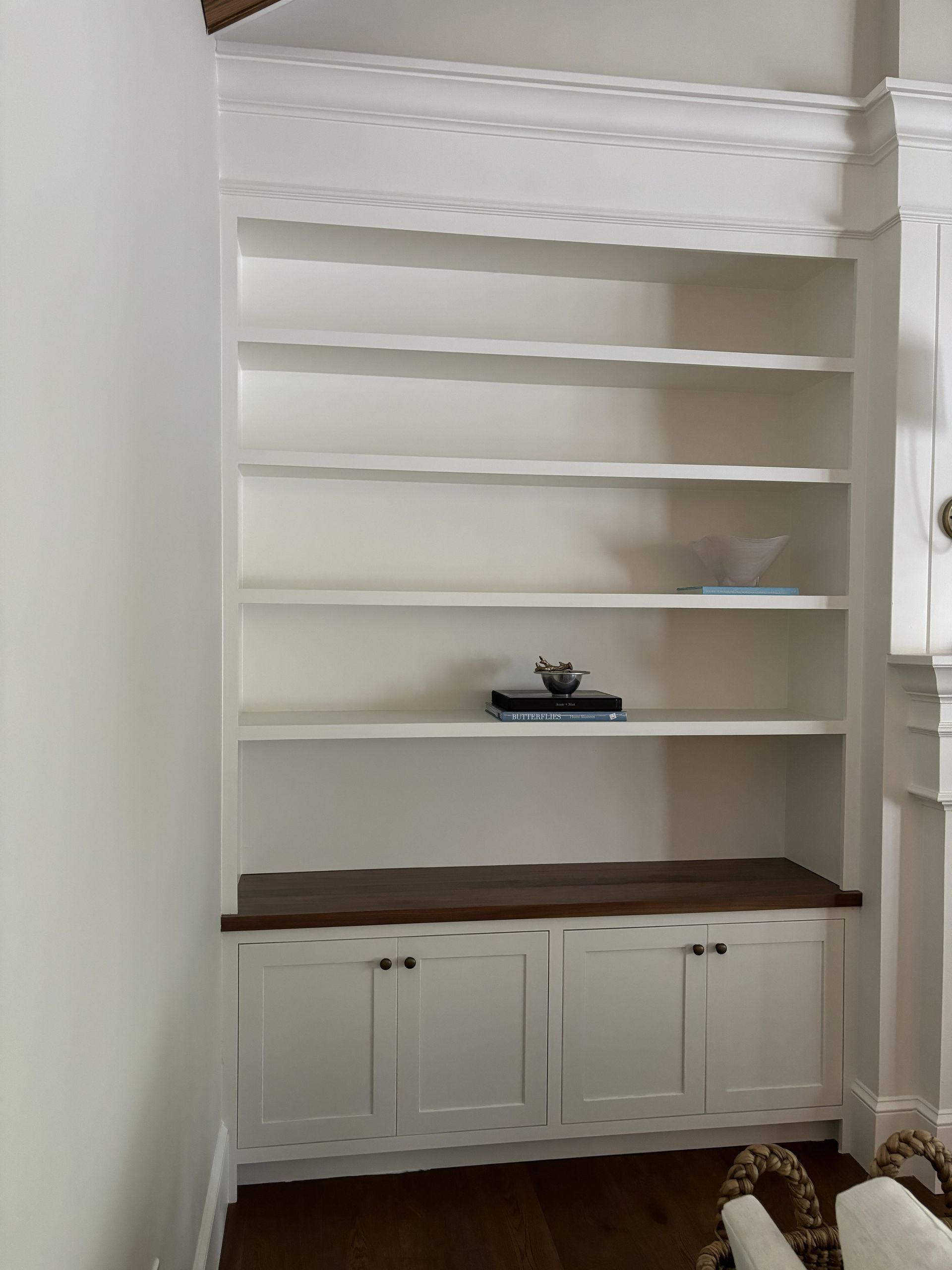 White built-in bookshelf with shelves and cabinets, stained wood seat, against a white wall.