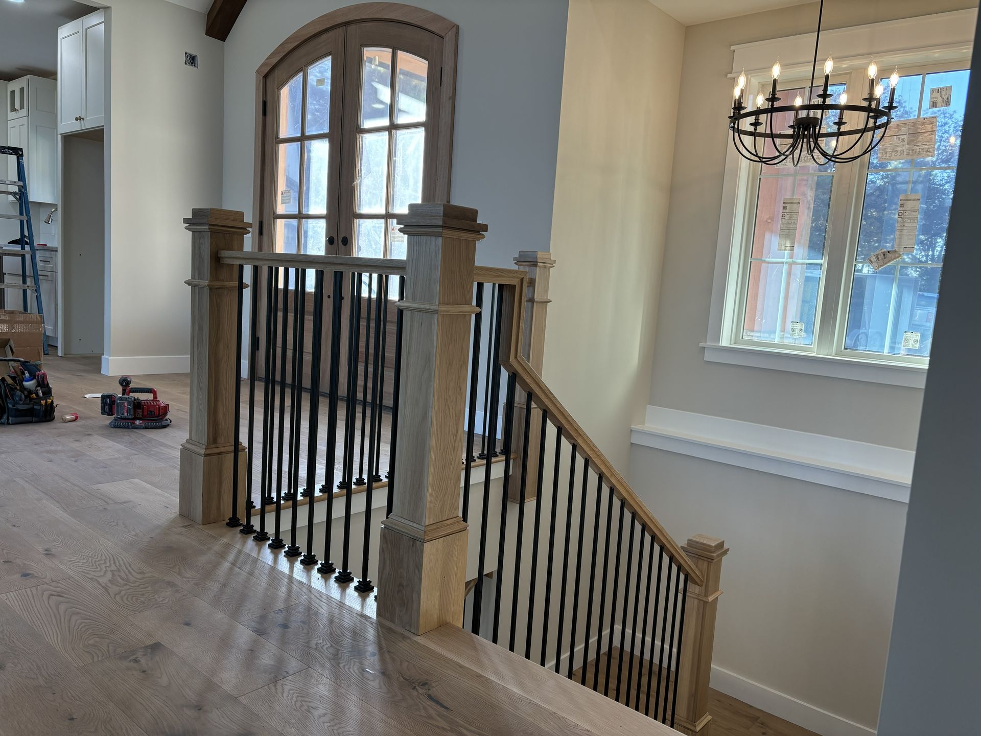 Staircase with wooden handrails, black iron balusters, and a chandelier, interior view.