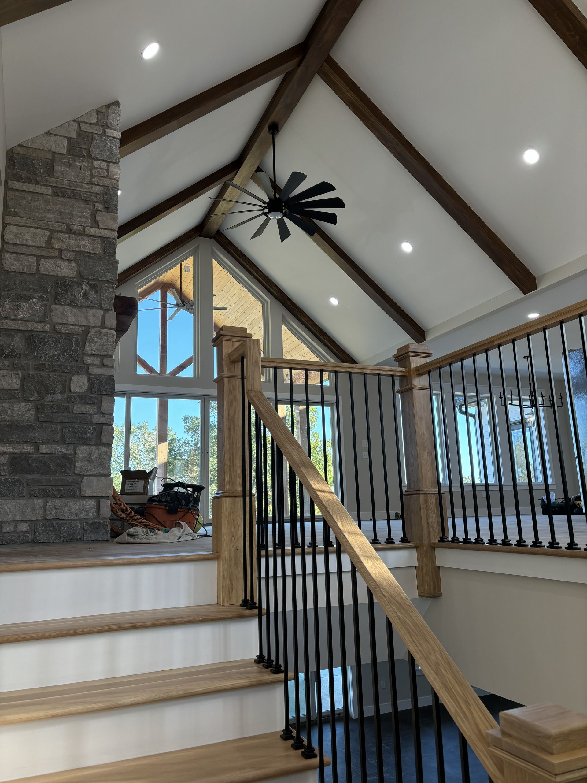 Staircase with wooden steps and railing, stone chimney, and high ceiling with exposed beams.