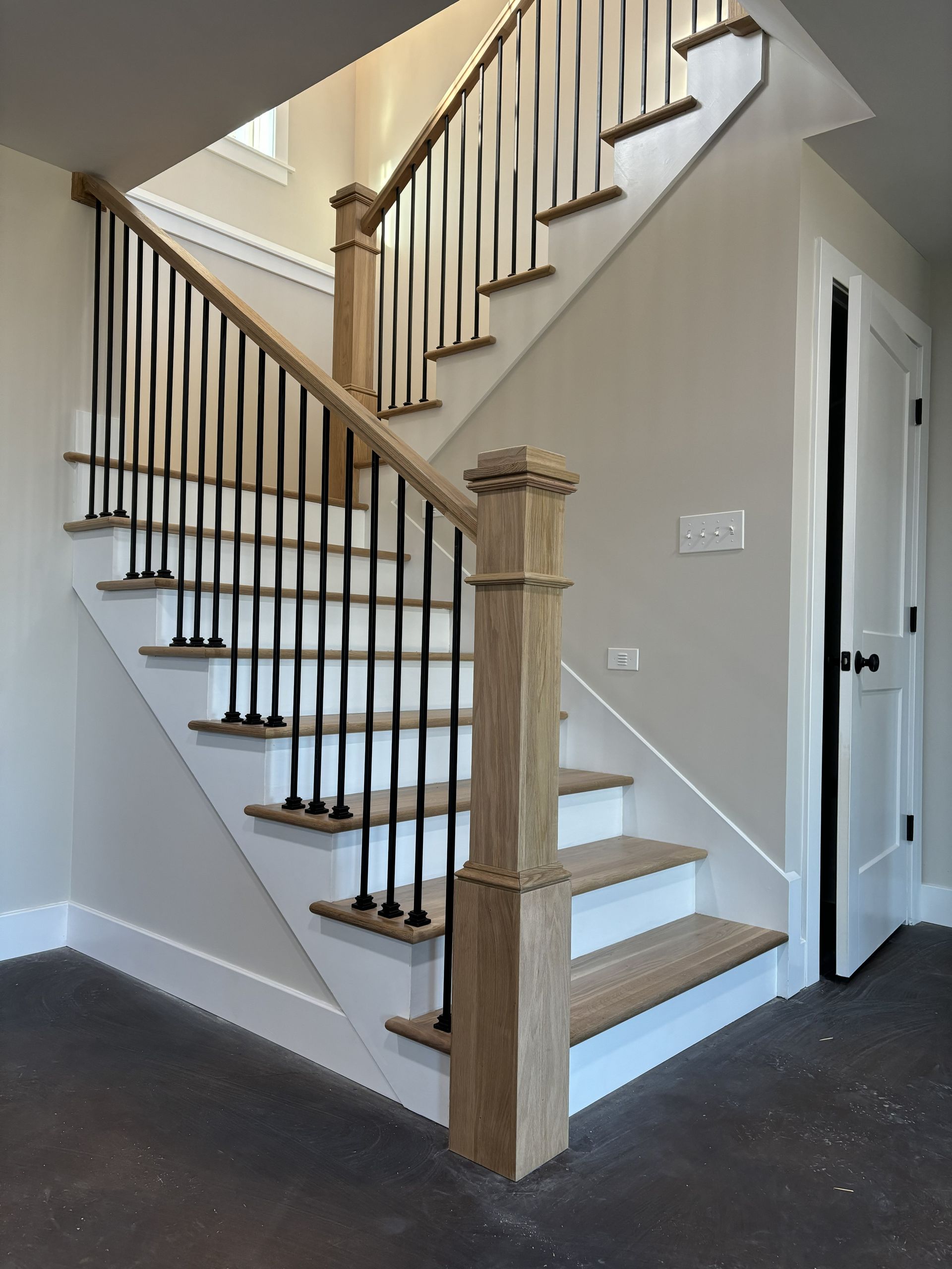 Staircase with wooden steps and railing, black iron balusters, and a white wall in a home interior.
