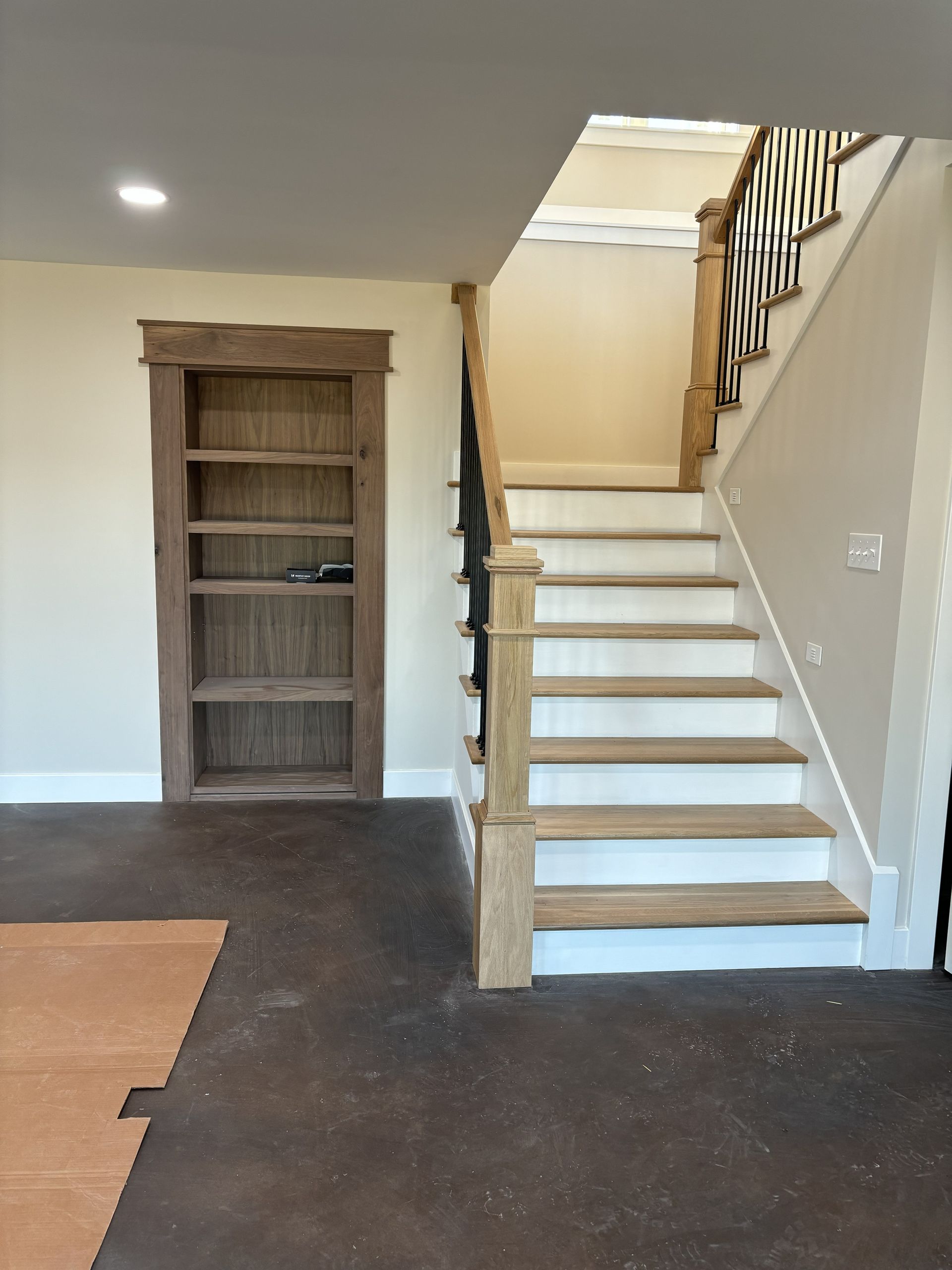 Interior view with staircase and built-in bookshelf. Light walls, wood stairs, dark floor.