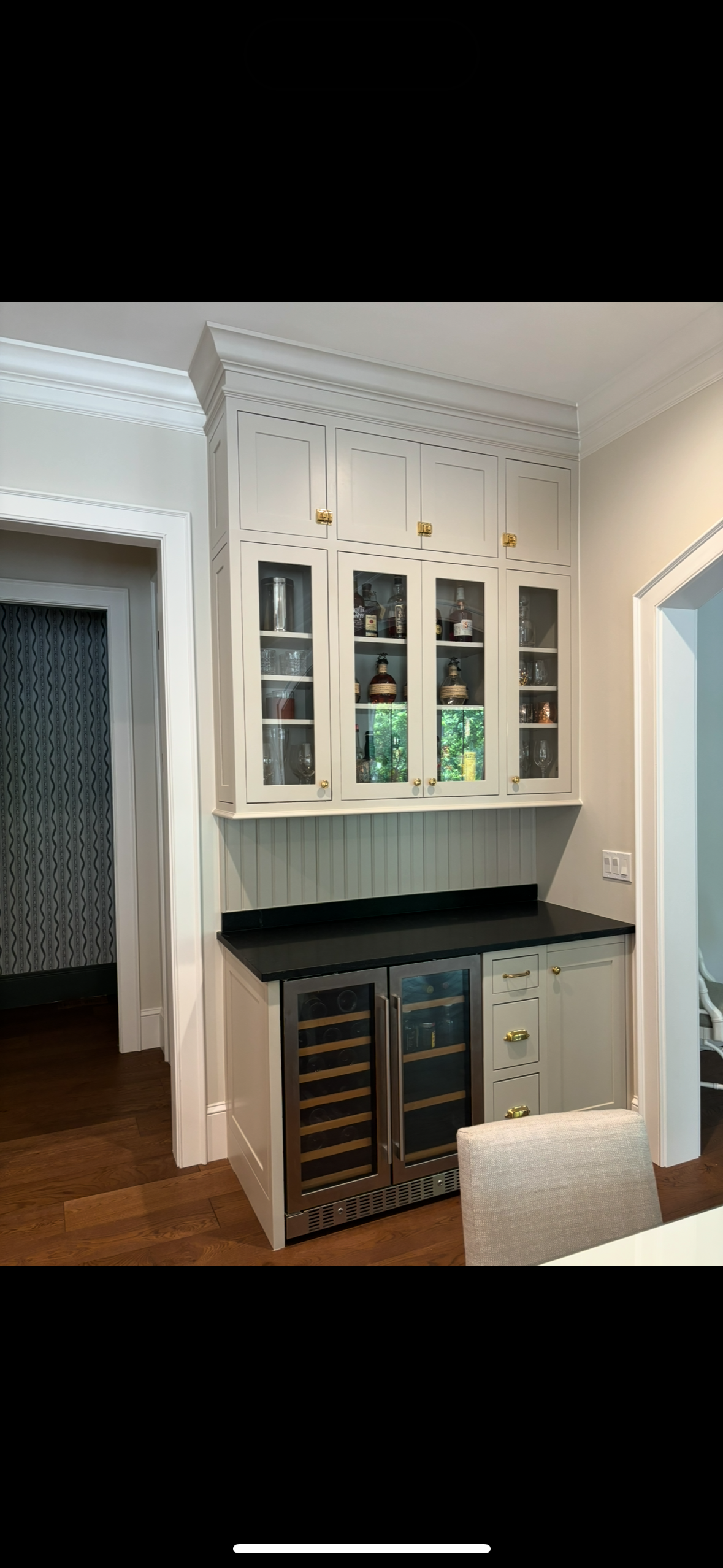 White built-in bar with glass-front cabinets, wine coolers, and black countertop in a room.