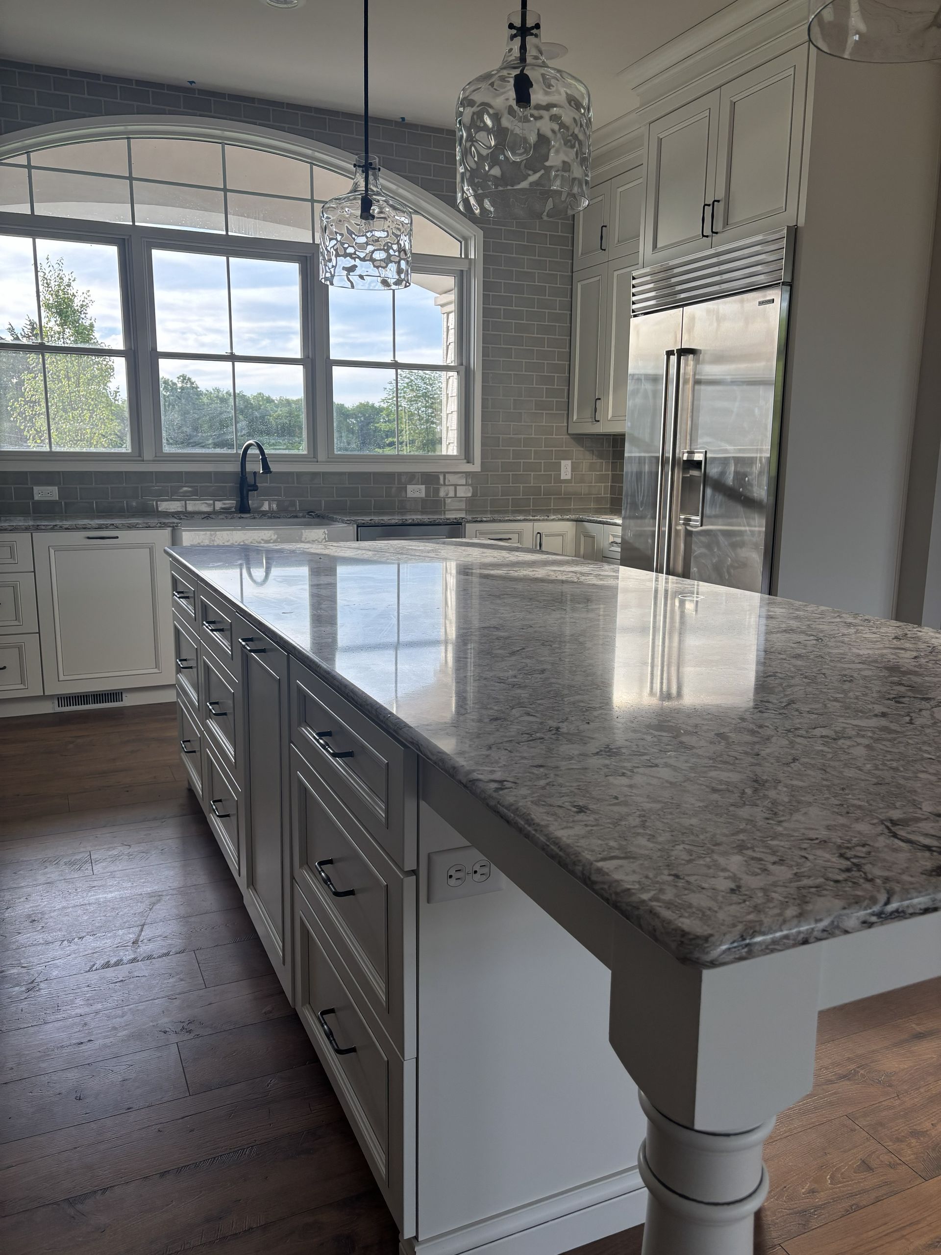 White kitchen with a large island, granite countertops, and two pendant lights.