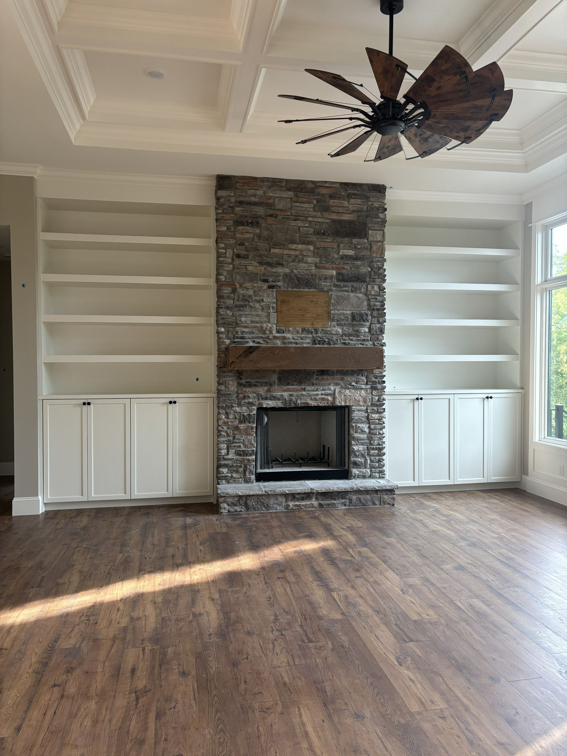 Living room with stone fireplace, built-in shelves, hardwood floor, and ceiling fan.