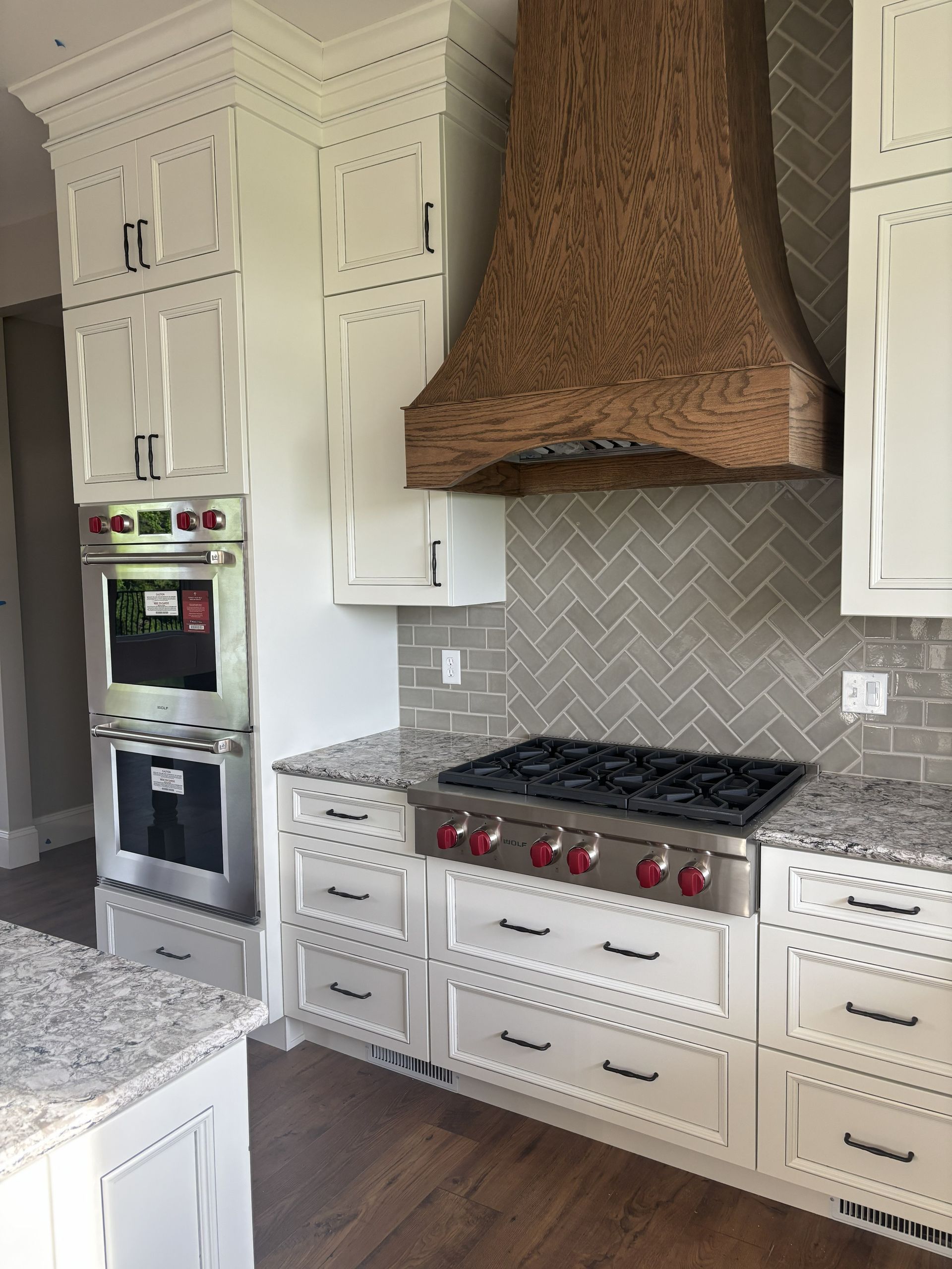 Kitchen with white cabinets, wood range hood, stainless steel stove, and granite countertops.