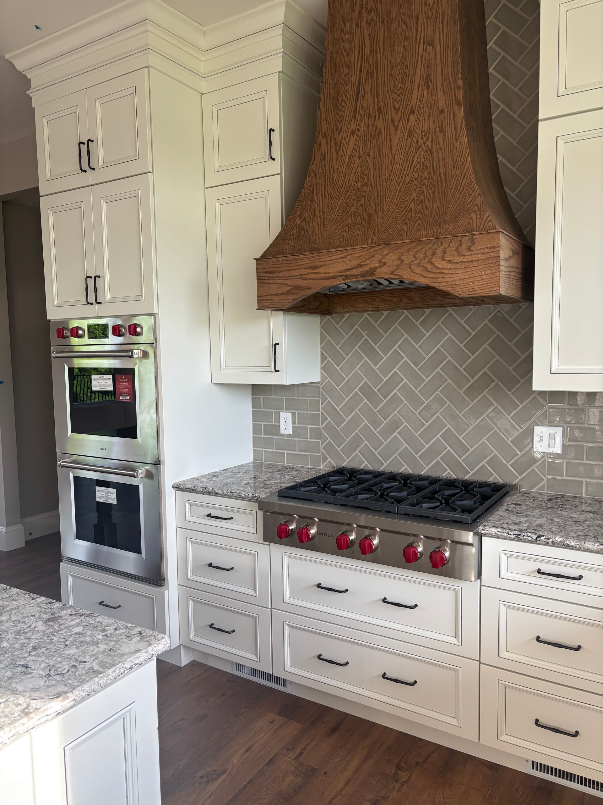 White kitchen cabinets with a wooden range hood, stainless steel appliances, and gray backsplash.