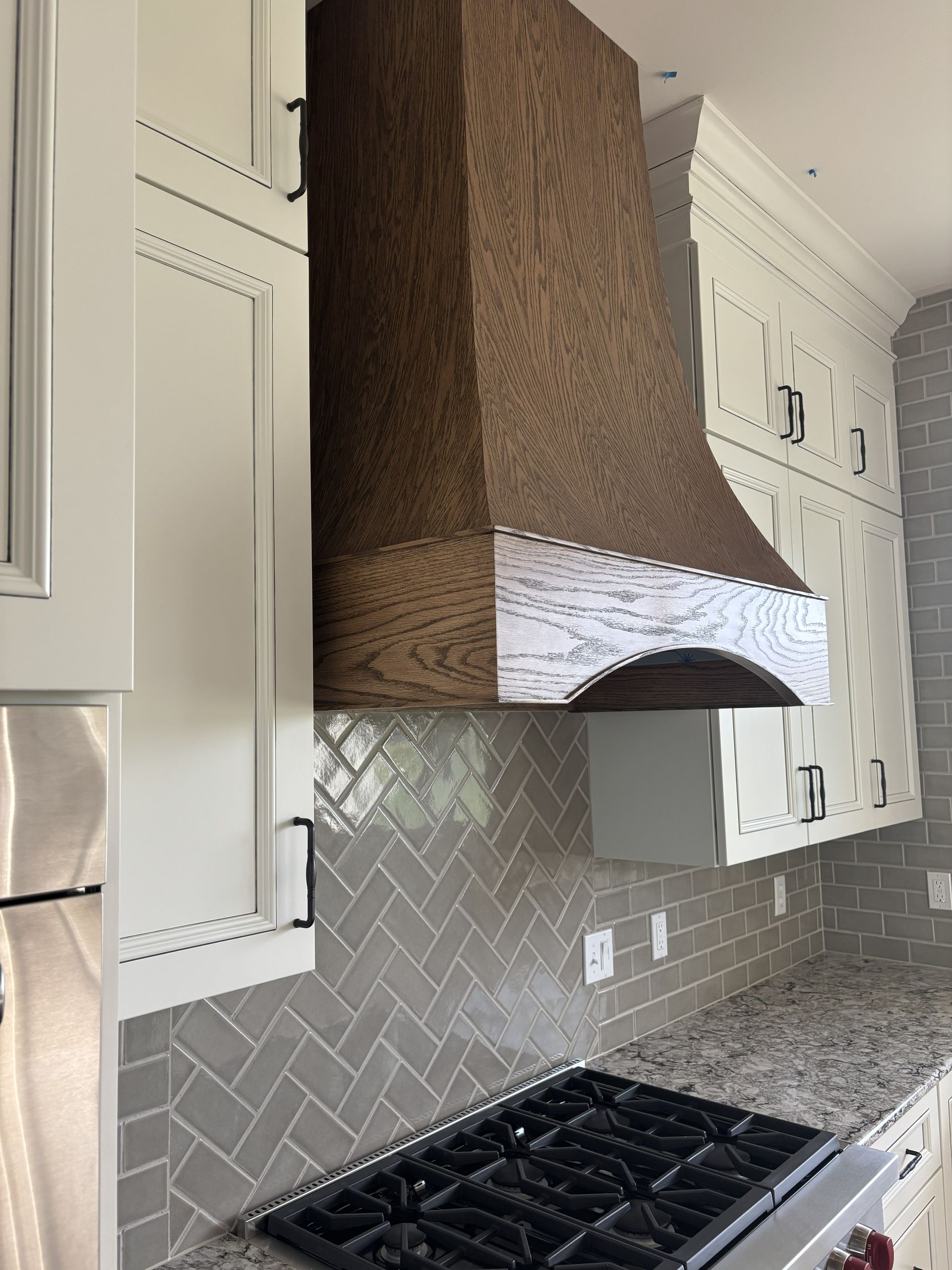 Kitchen with brown wooden range hood, white cabinets, gray tile backsplash, and gas stovetop.