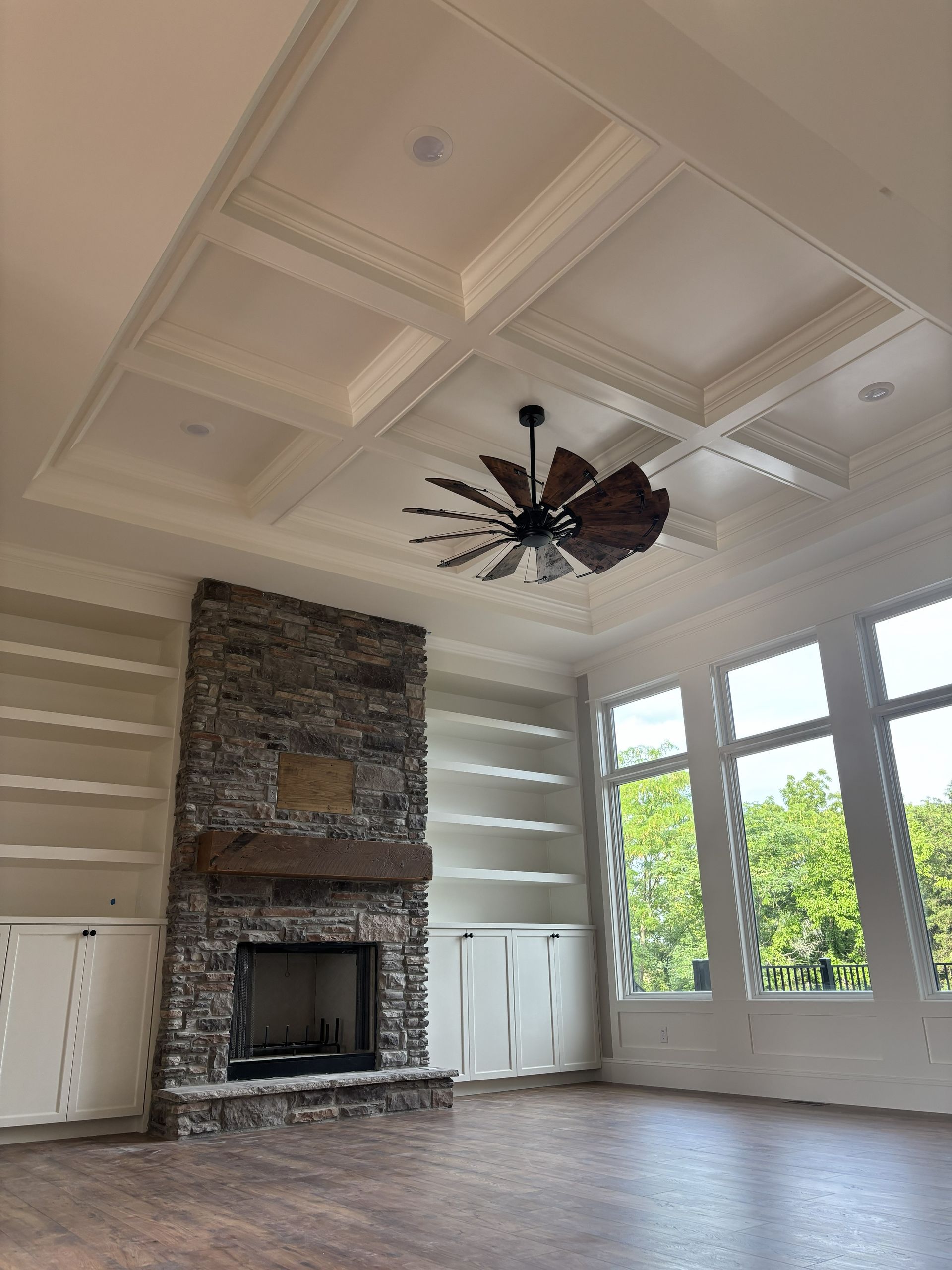 Living room with a stone fireplace, built-in shelves, and a decorative ceiling with a ceiling fan.
