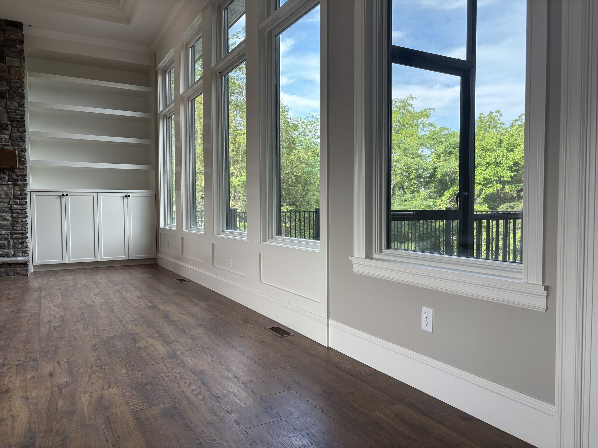 Room interior with large windows, hardwood floors, and a stone accent wall.