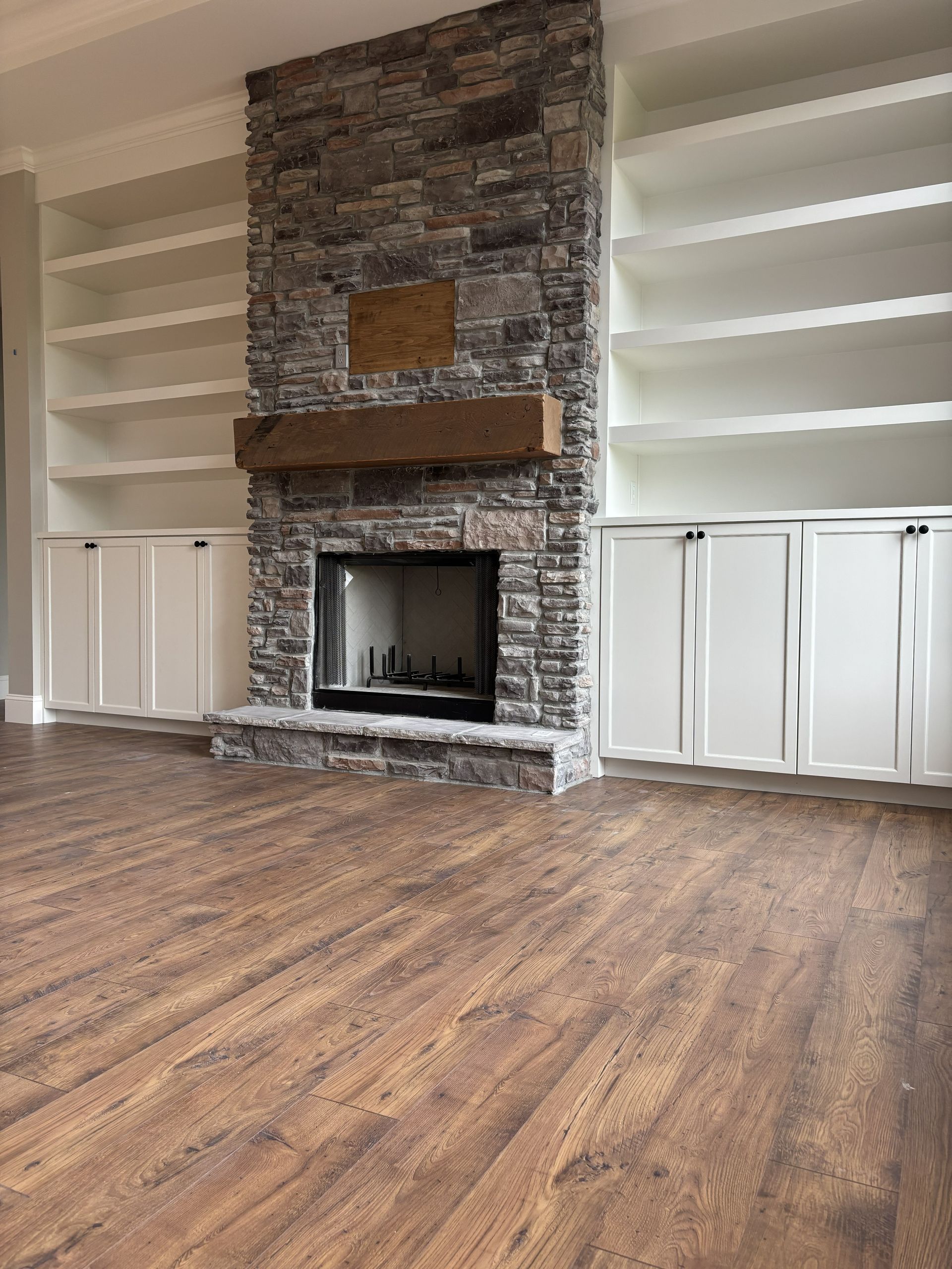 Stone fireplace with a wooden mantle and built-in white shelves and cabinets. Wooden floors.