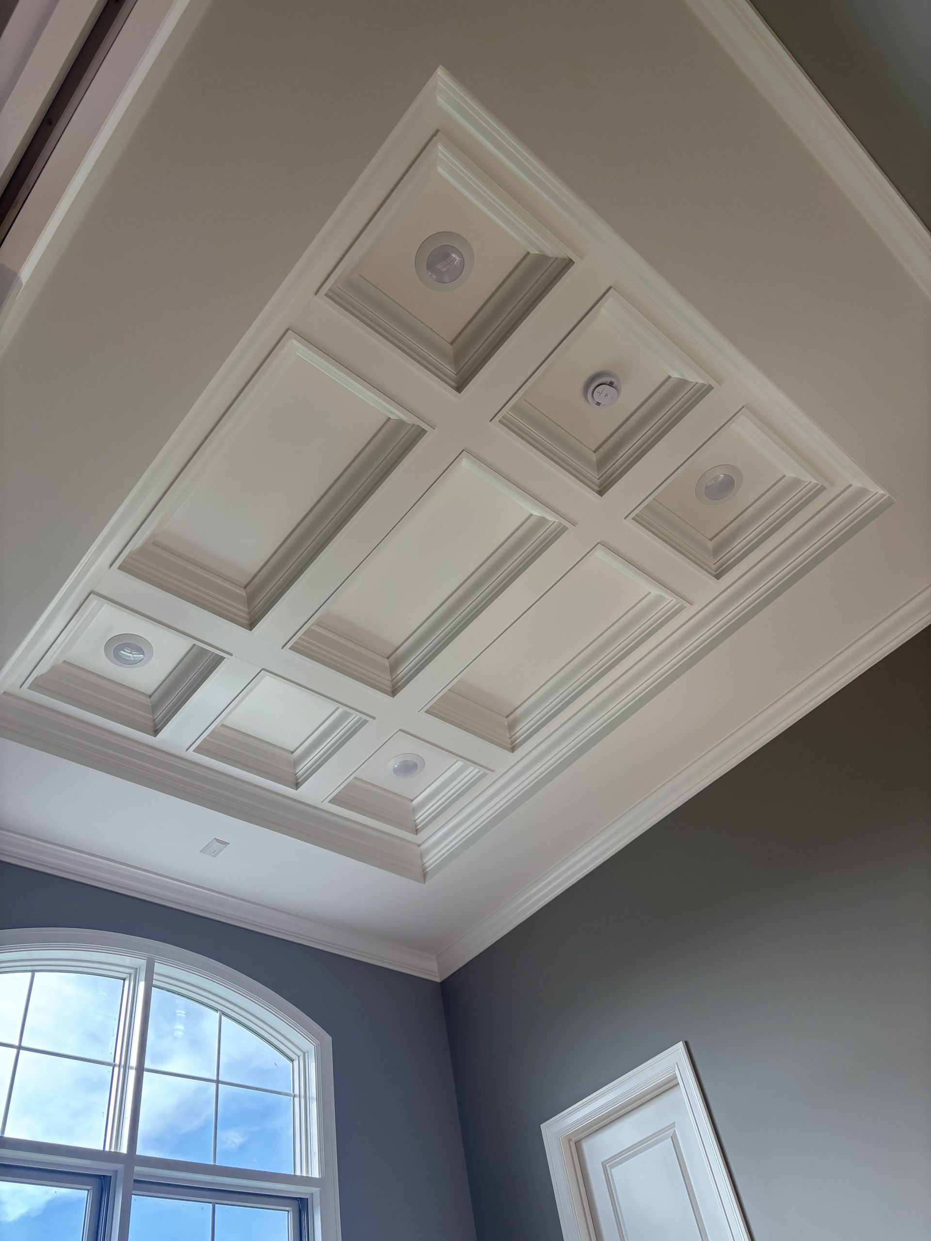A decorative white coffered ceiling with recessed lighting above a window.