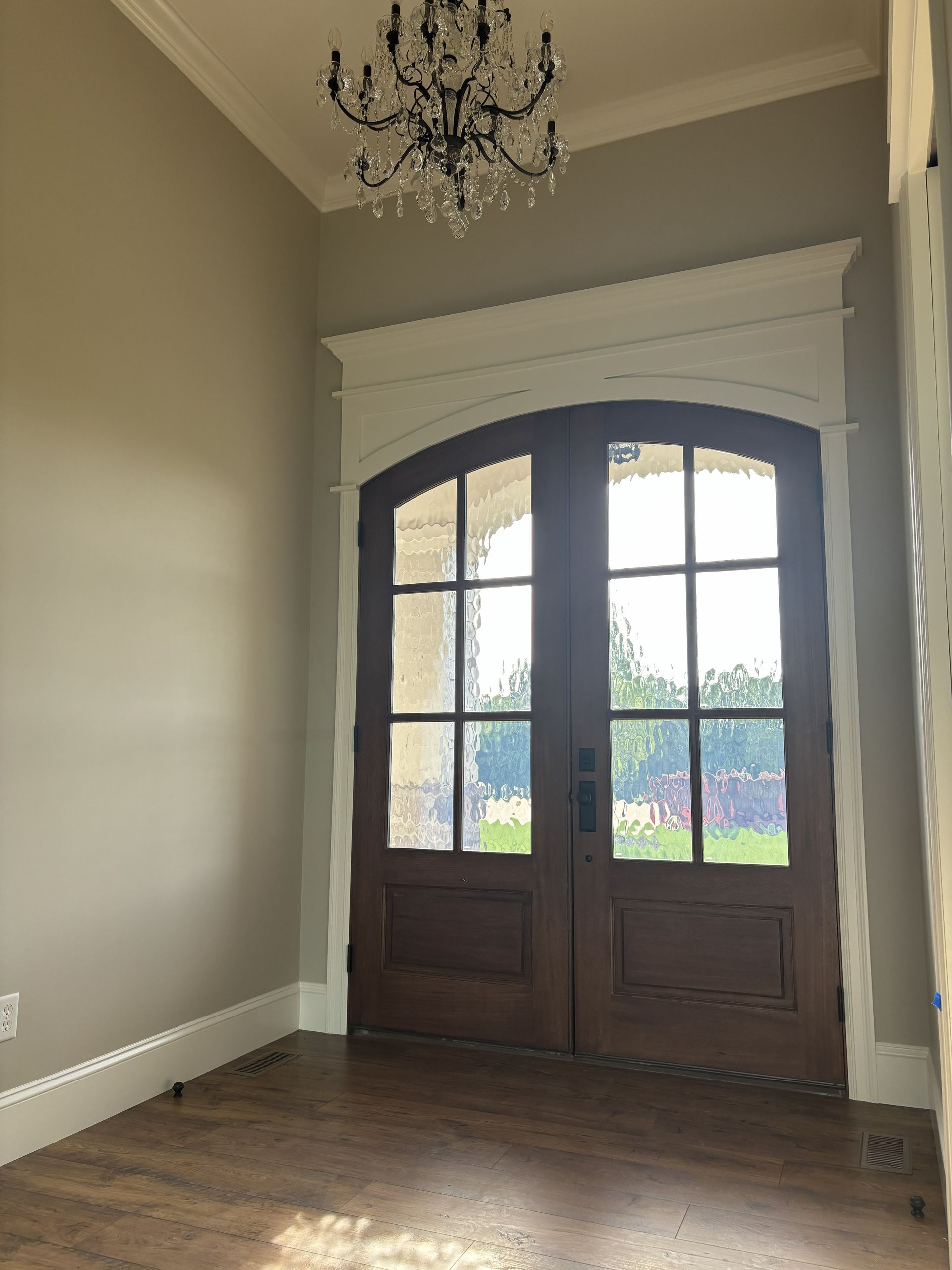 Wooden double doors with arched tops, six glass panes each, and a chandelier, framed by white trim.