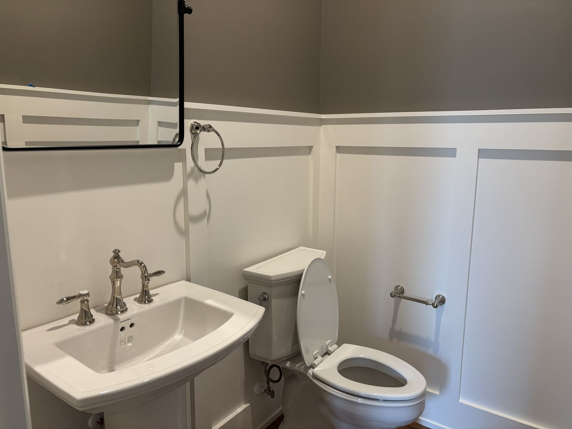 White-walled bathroom with sink, toilet, and towel rack. Gray walls above the wainscoting.