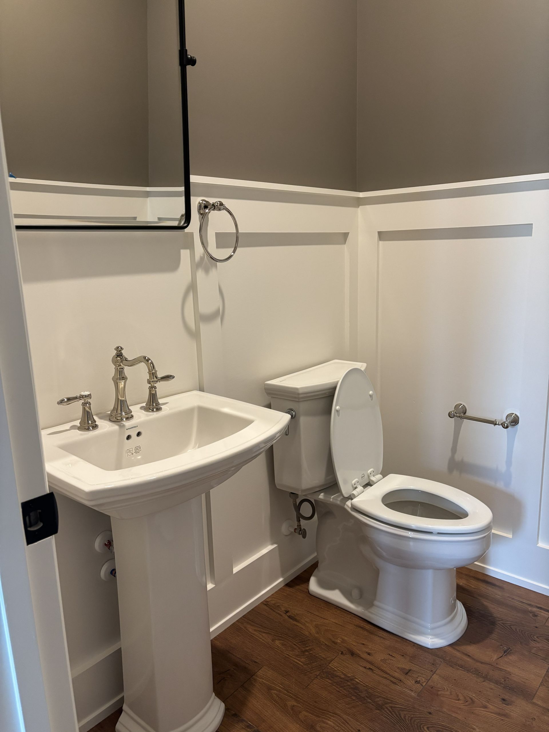 White pedestal sink, toilet, and wainscoting in a small bathroom with gray and white walls.