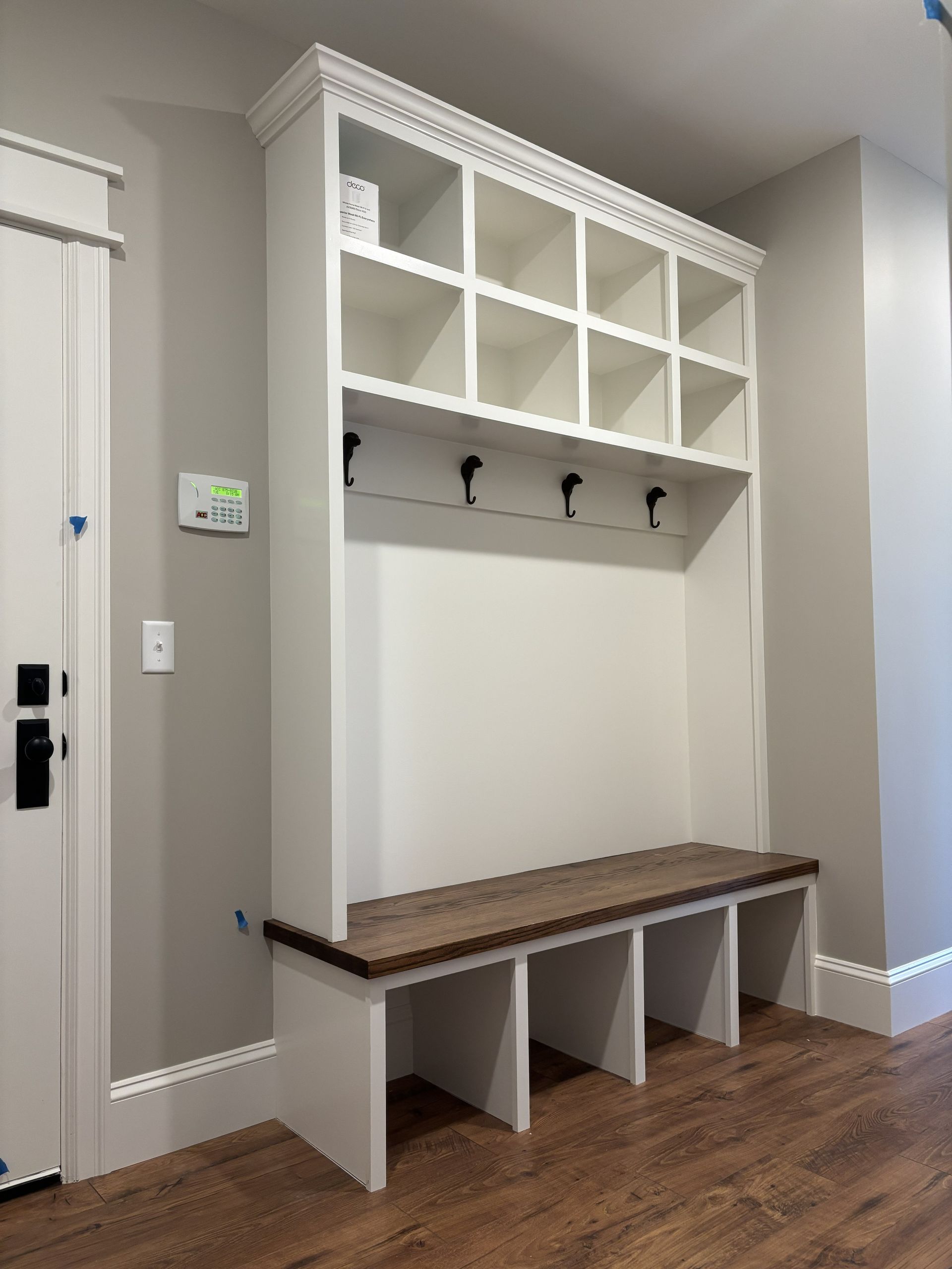 White built-in entryway bench with cubbies, hooks, and a wooden seat.