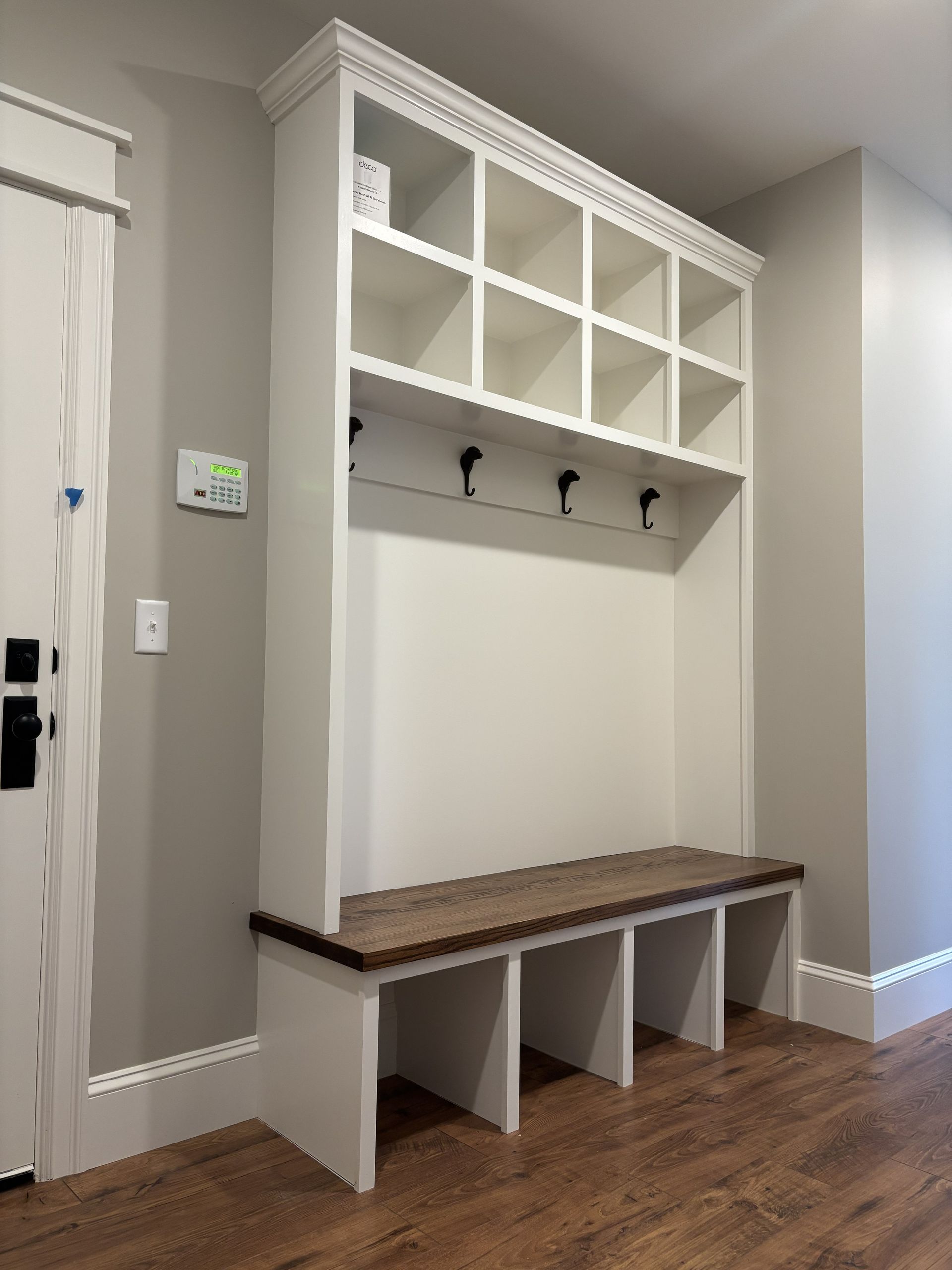 White built-in storage unit with cubbies, hooks, and a bench with a wooden top in a hallway.