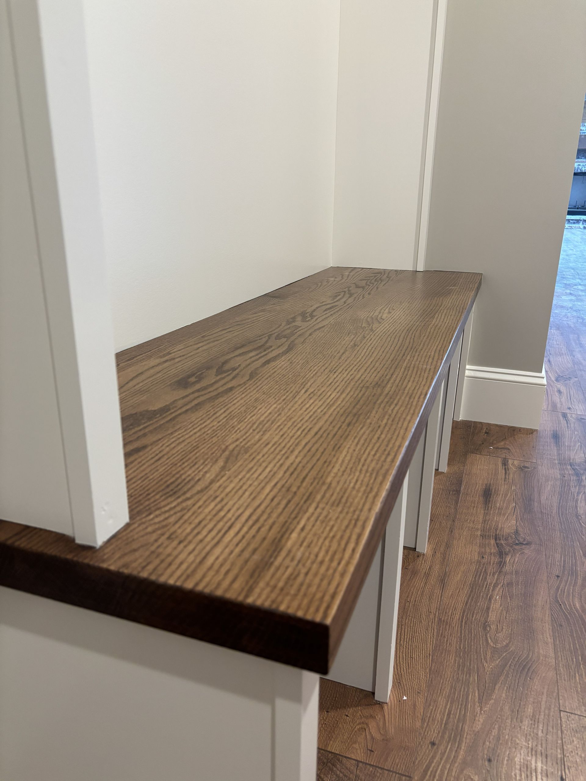 Wooden bench built into a white wall unit, with a dark wood-grained top, and white legs.