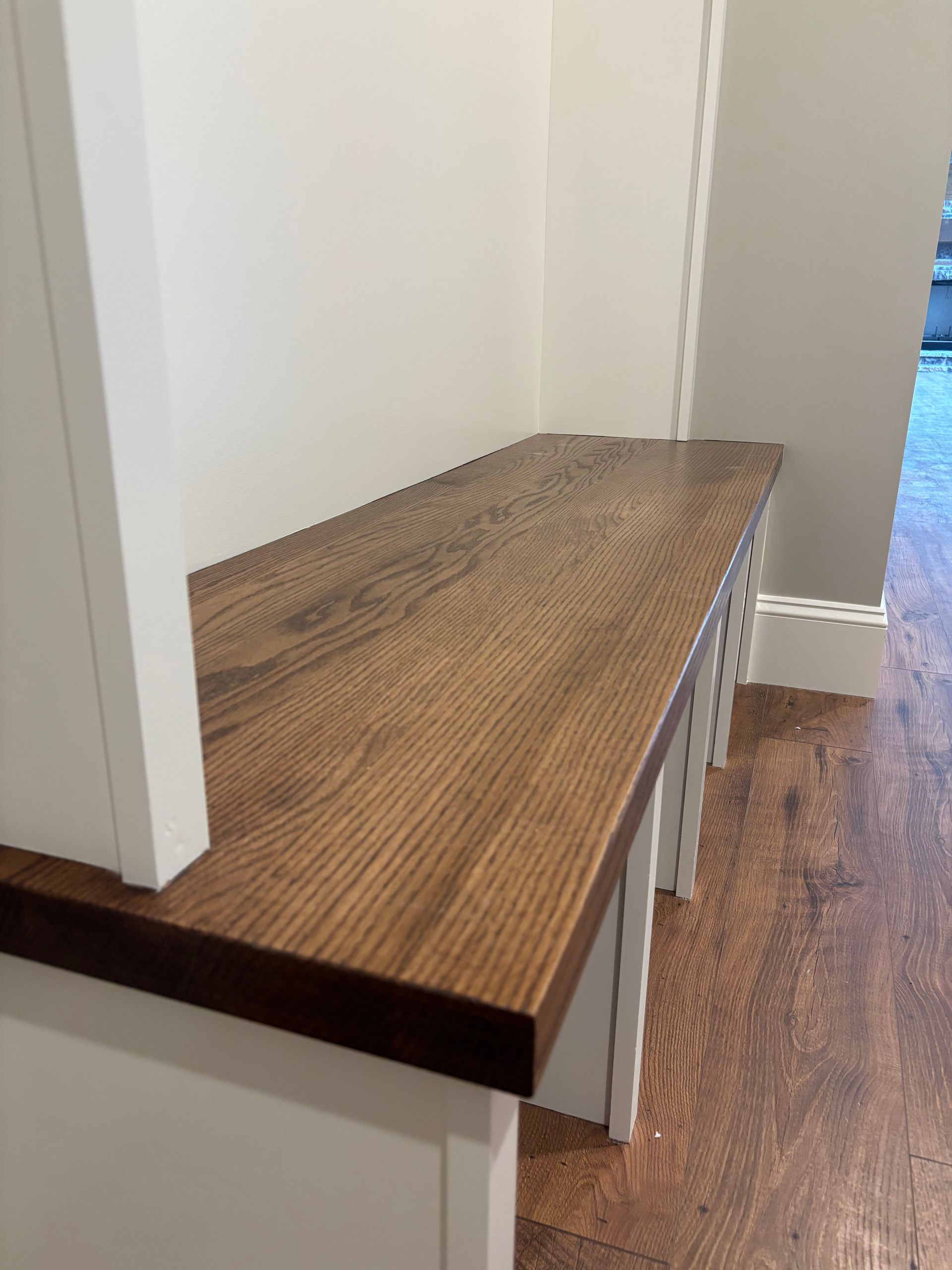 Wooden bench with a white base and a dark wooden top, in an entryway.
