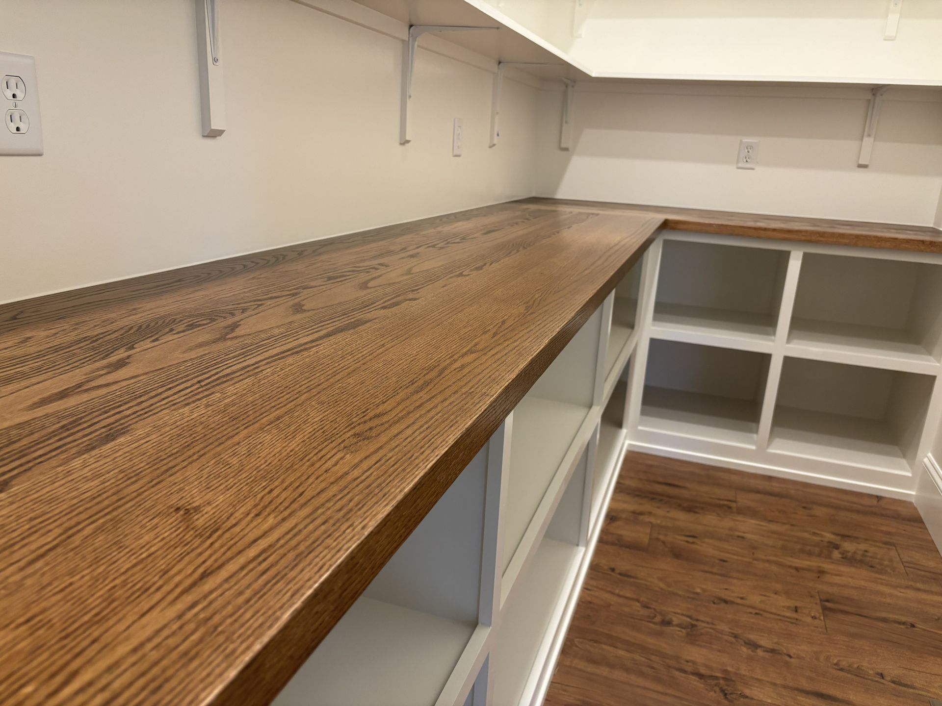 L-shaped pantry with wood-look countertops and white shelving. Wall outlet visible.