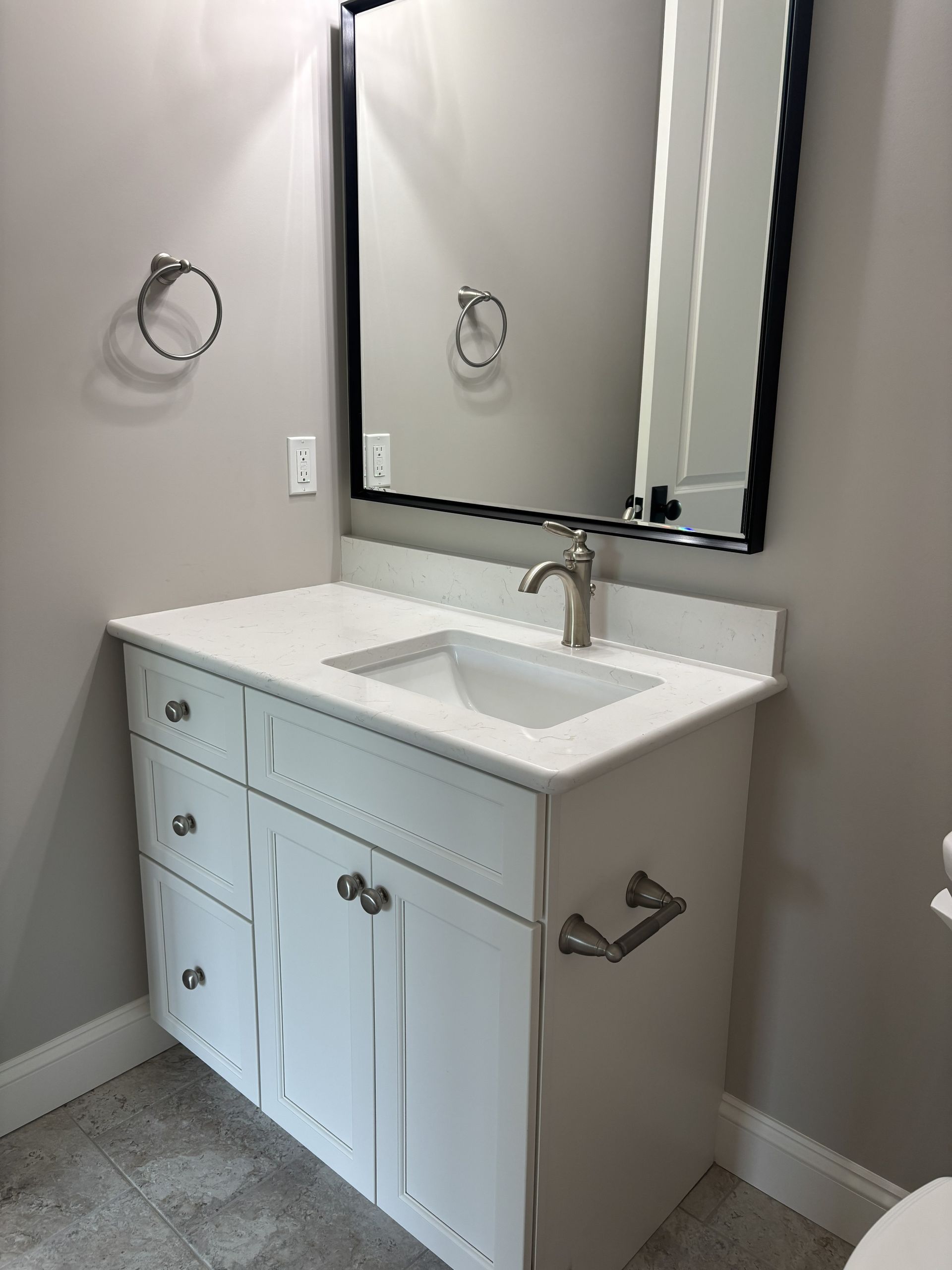 White bathroom vanity with marble countertop, stainless steel faucet, and mirror.