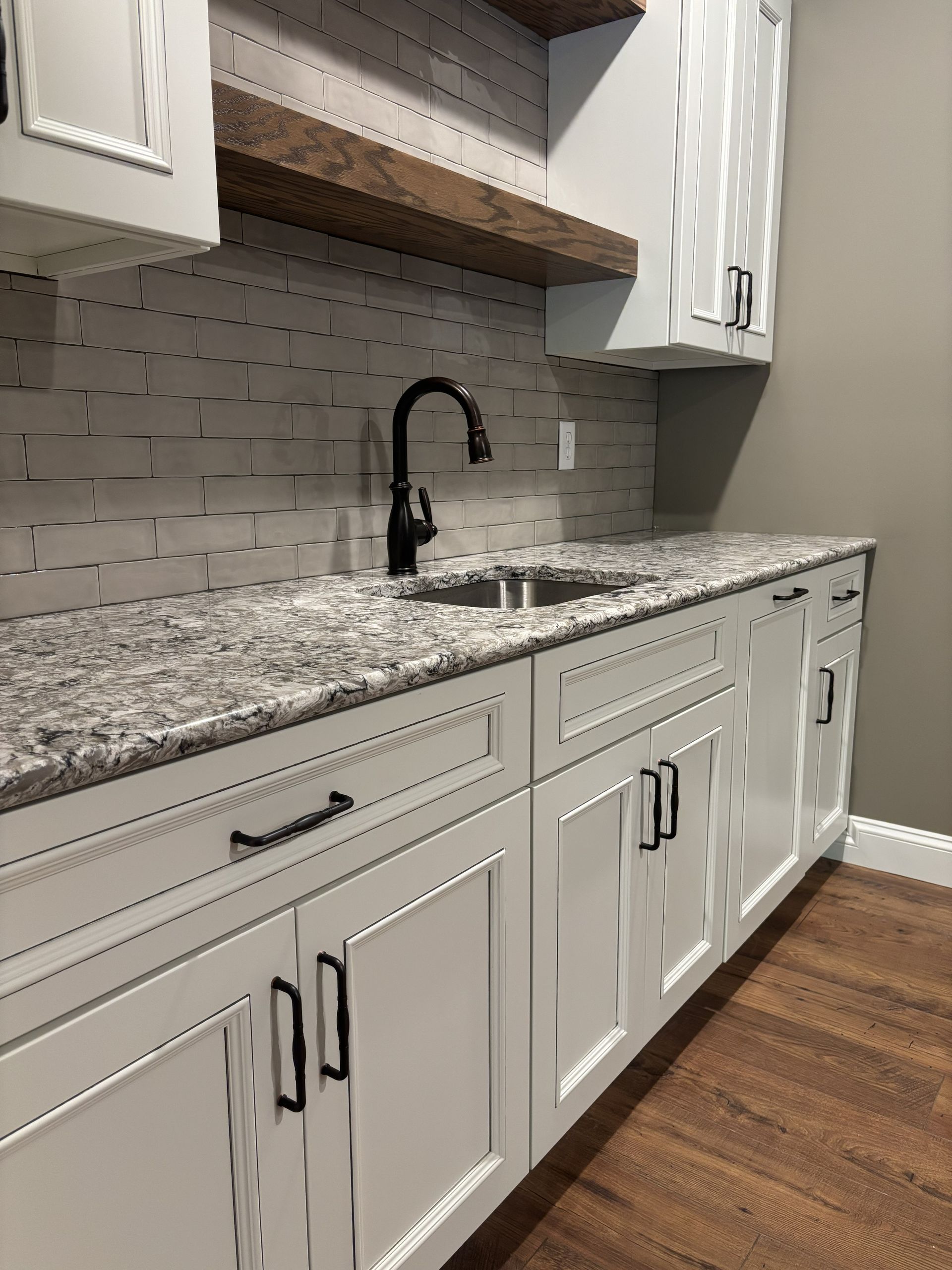 White kitchen cabinets with black hardware, granite countertop, and dark faucet.