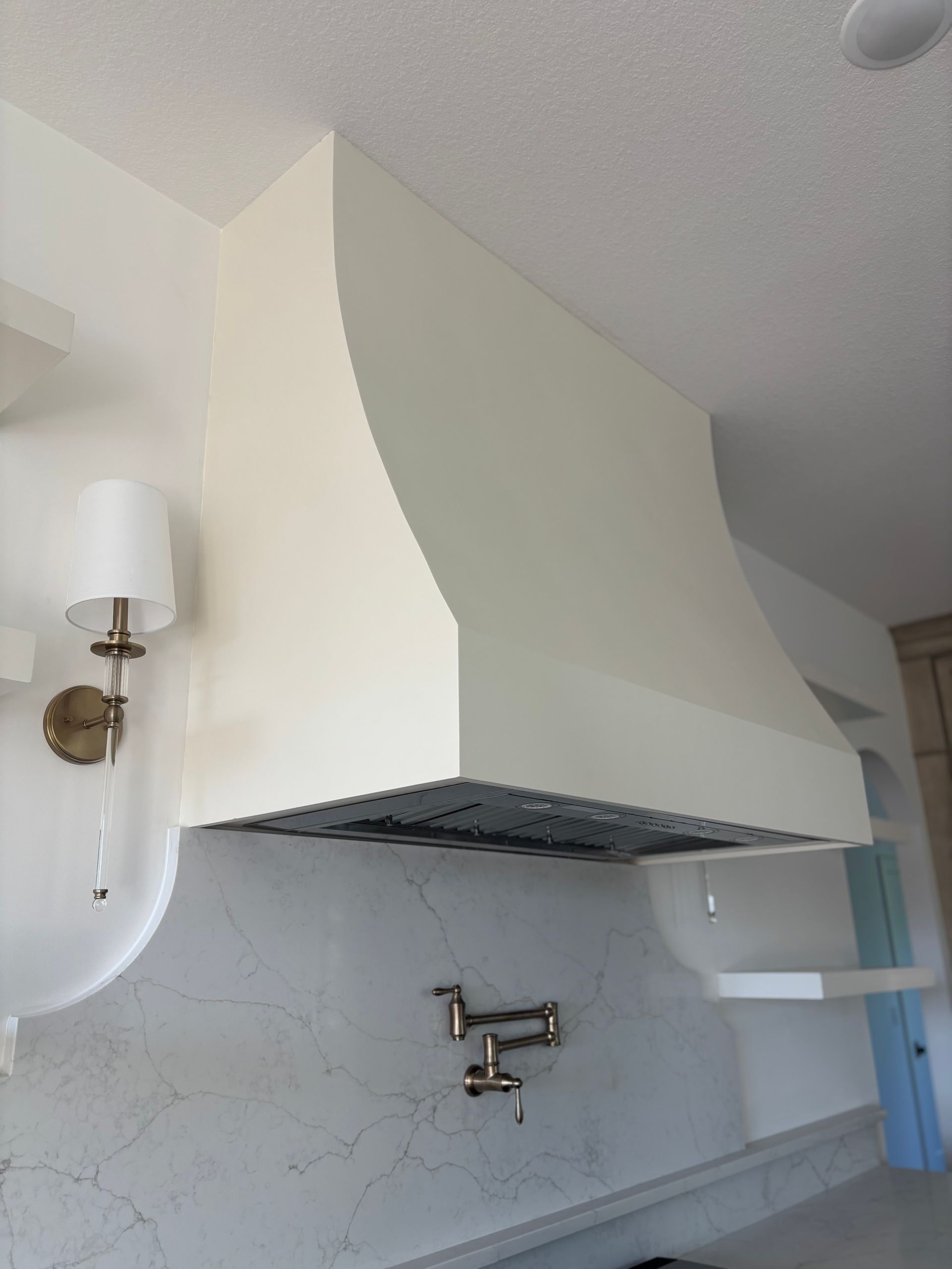 Off-white kitchen range hood with curved sides above stovetop and a pot filler faucet.
