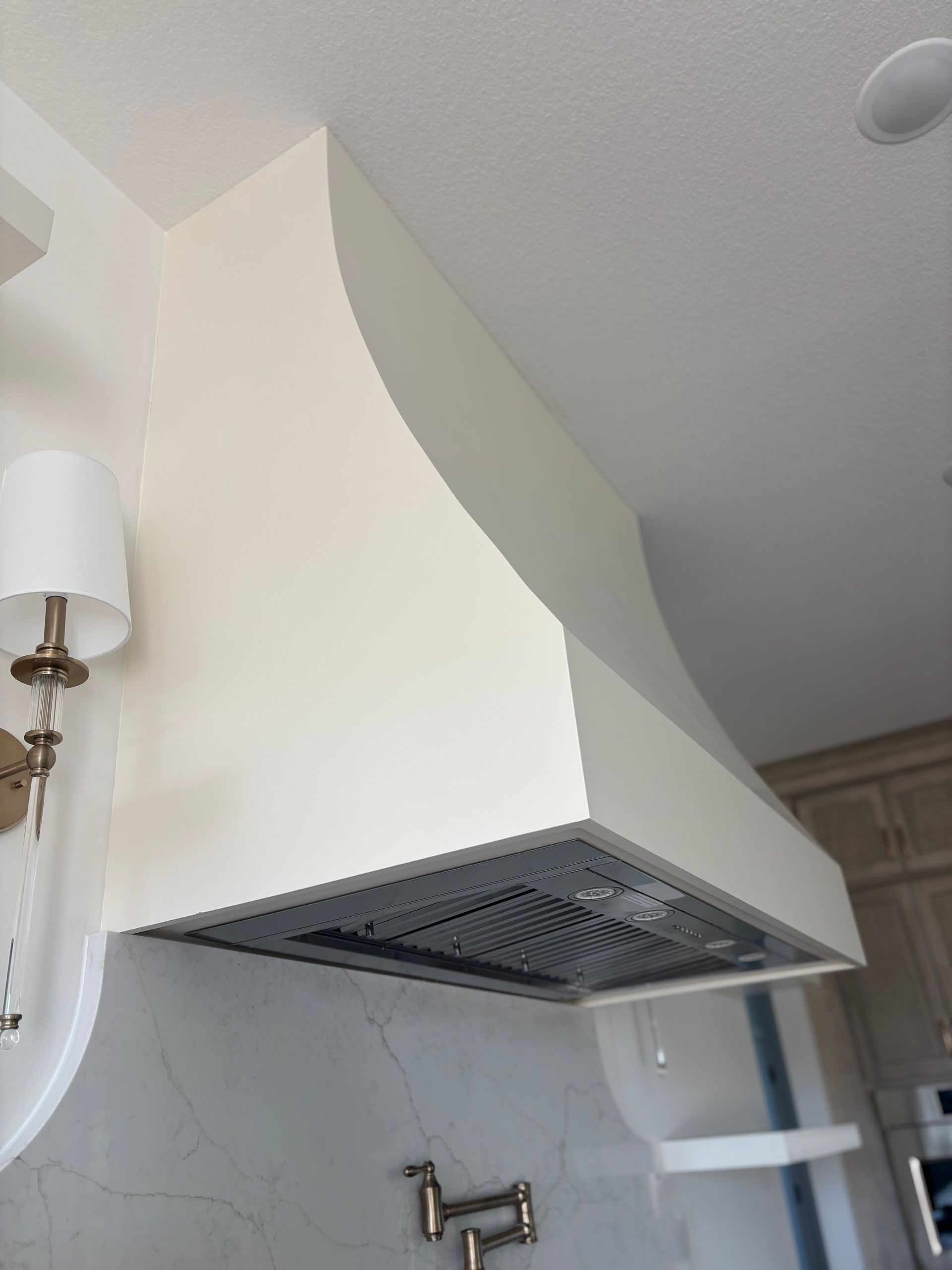 Cream-colored kitchen range hood with a curved design, mounted above a cooktop.