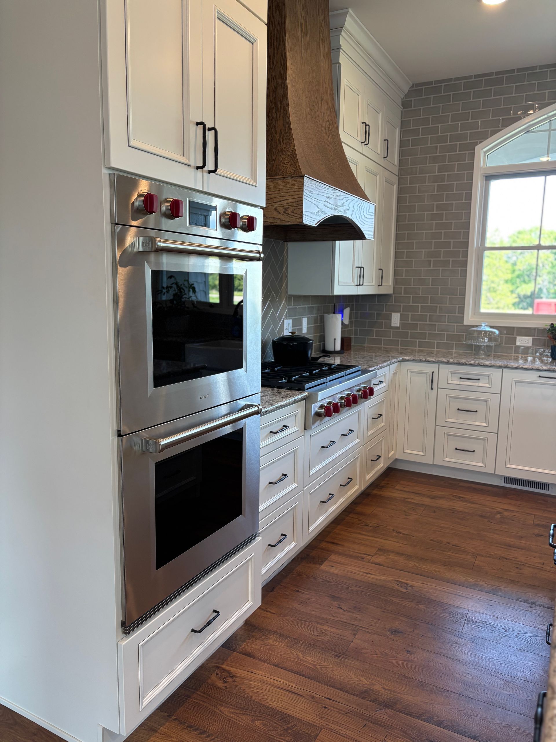 White kitchen with oven, stovetop, and brick backsplash. Wooden floor and cabinets.