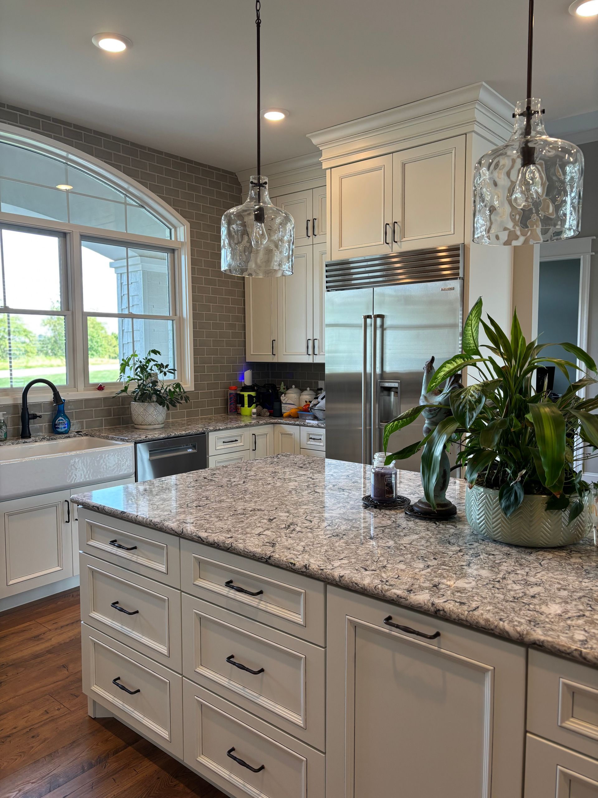 White kitchen with island, granite countertop, two hanging lights, and large stainless steel refrigerator.