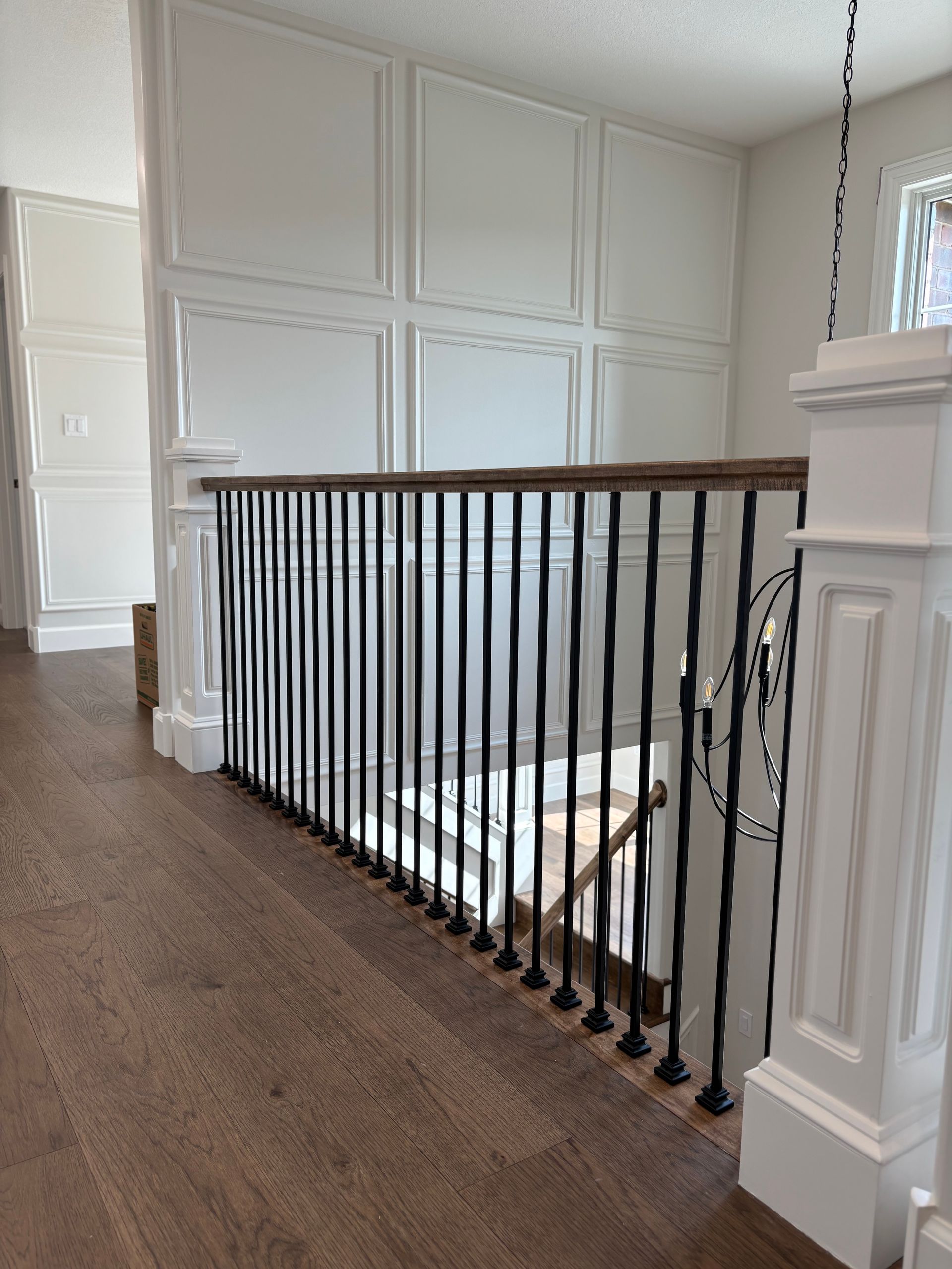Hallway with wooden floor, white panel wall, black wrought iron railing, and staircase.