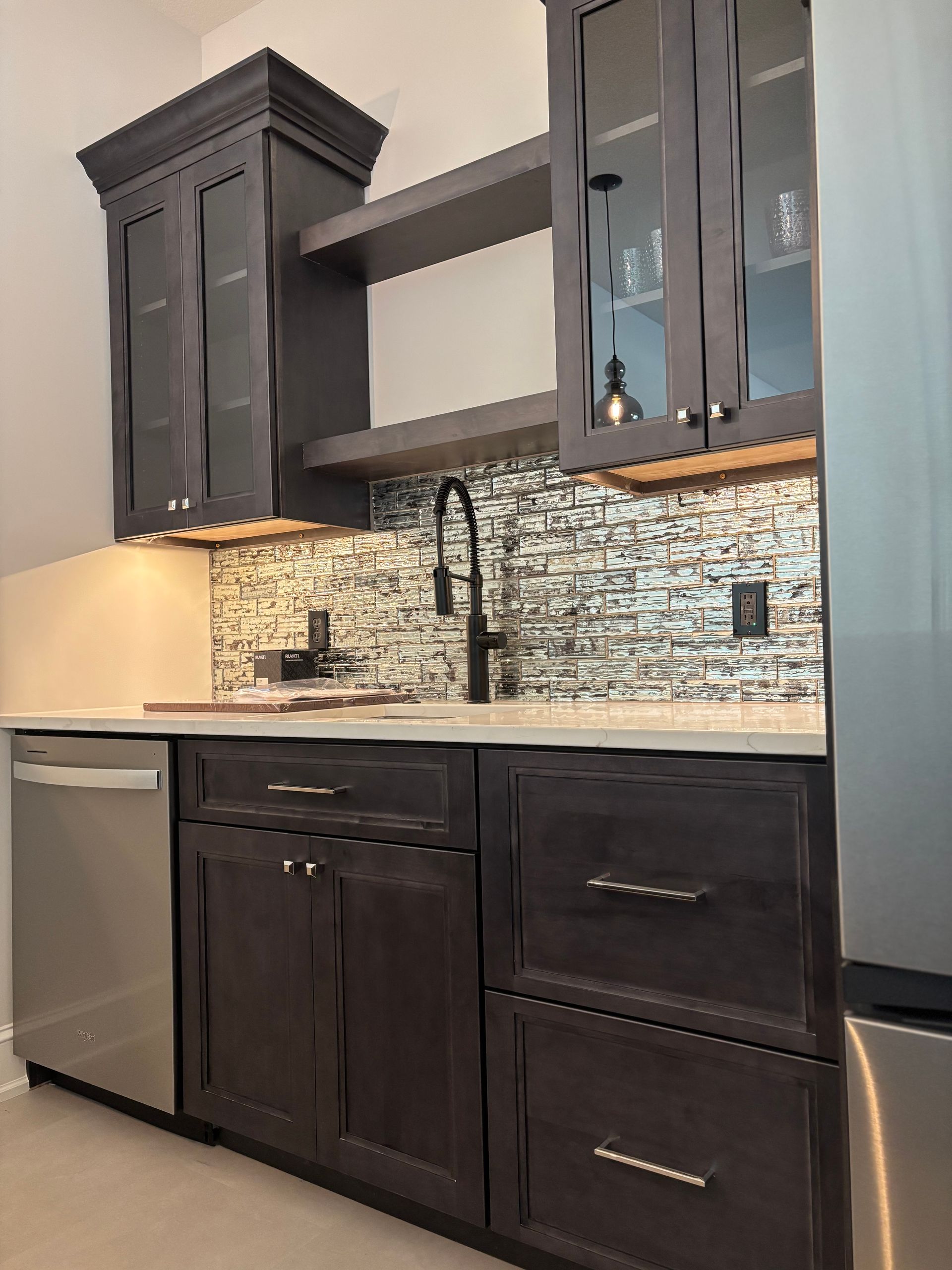 Dark stained kitchen bar area with dishwasher, cabinets, backsplash, and open shelving.
