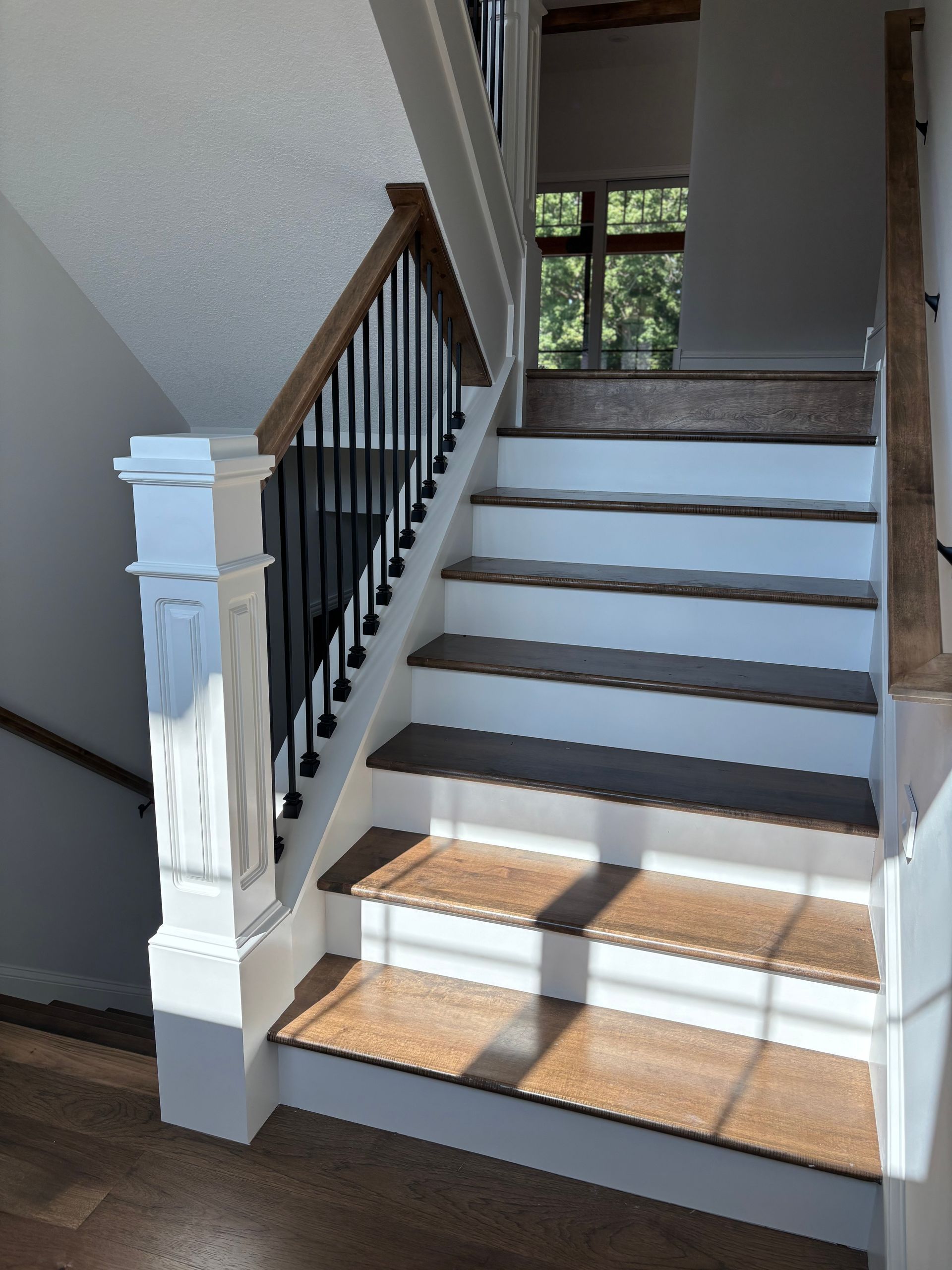 Wooden staircase with white risers, wooden treads, black spindles, and wooden handrails.