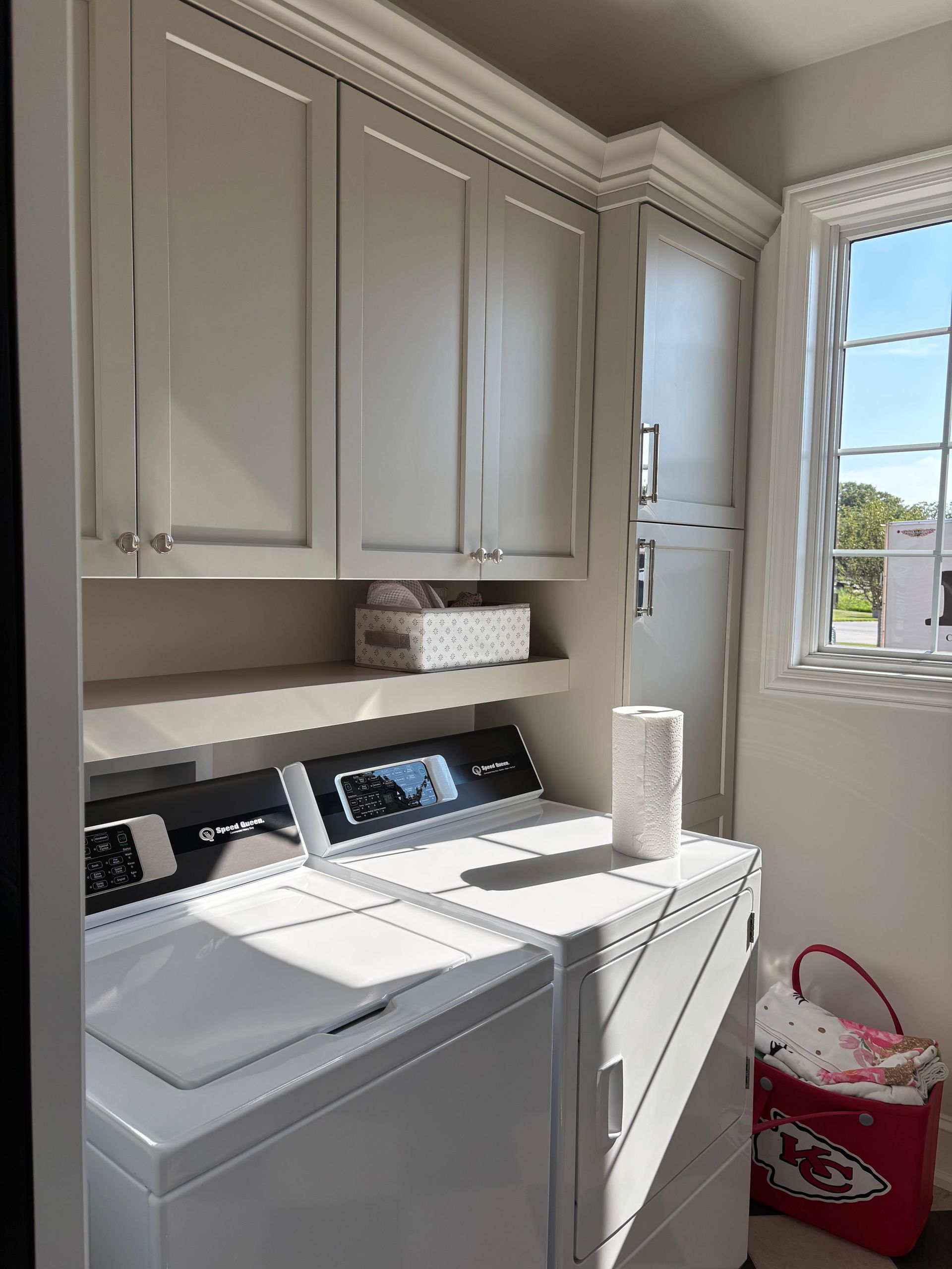 Laundry room with white cabinets, washer, dryer, and a window with sunlight.