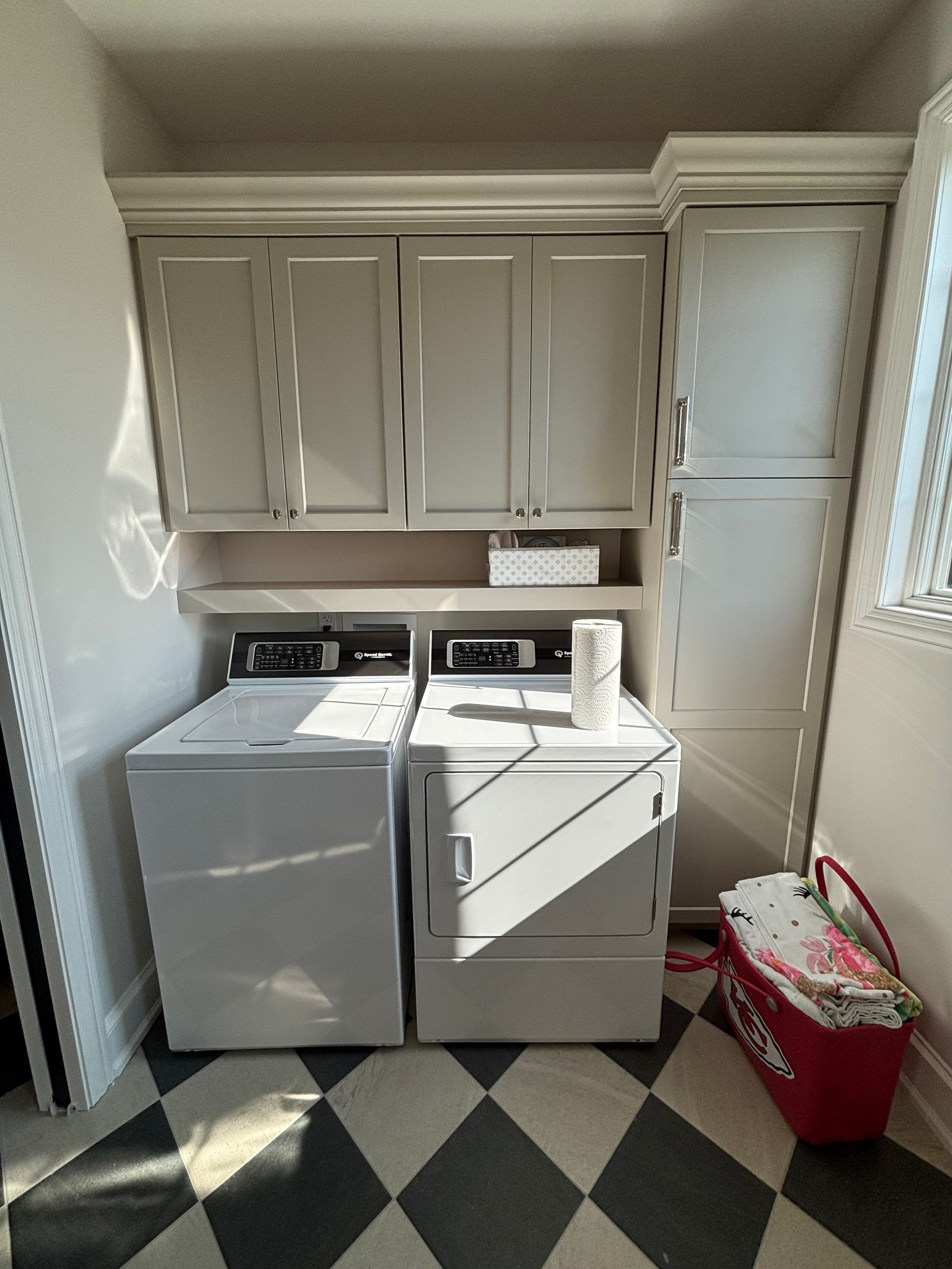 Laundry room with white washer and dryer, grey cabinets, and black and white checkered floor.