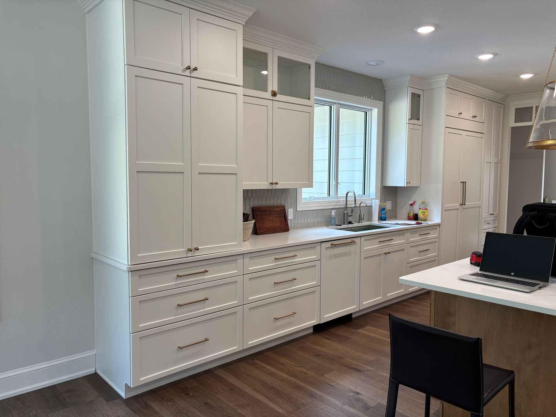 White kitchen cabinets with drawers and appliances. Light countertop, window, and wood floor.