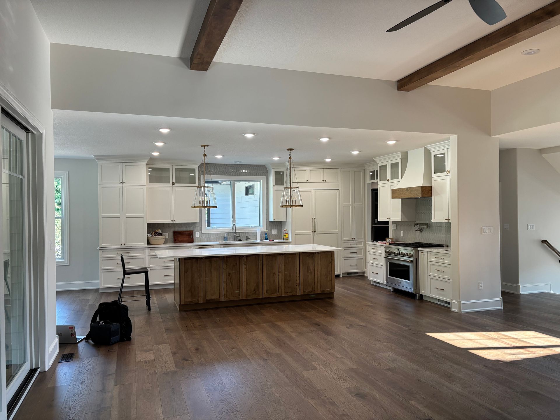 Spacious kitchen with white cabinets, dark wood island and floors, beams, and large windows.