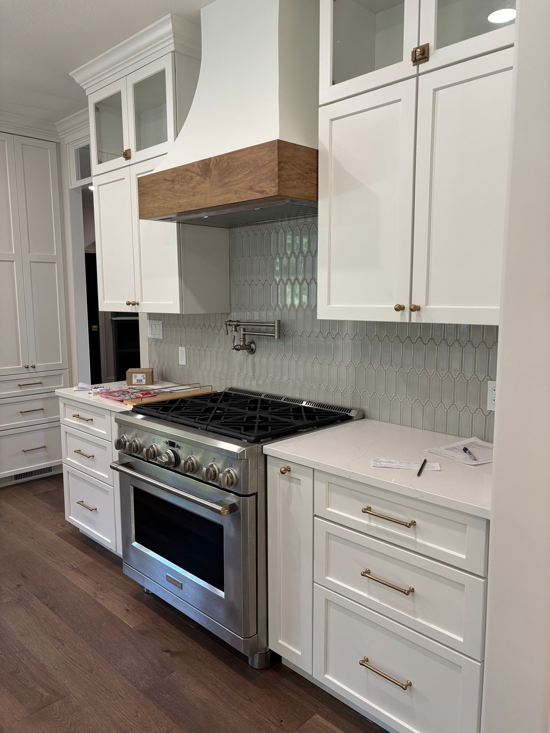 White kitchen with stainless steel stove, wood hood, light tile backsplash, and cabinets.