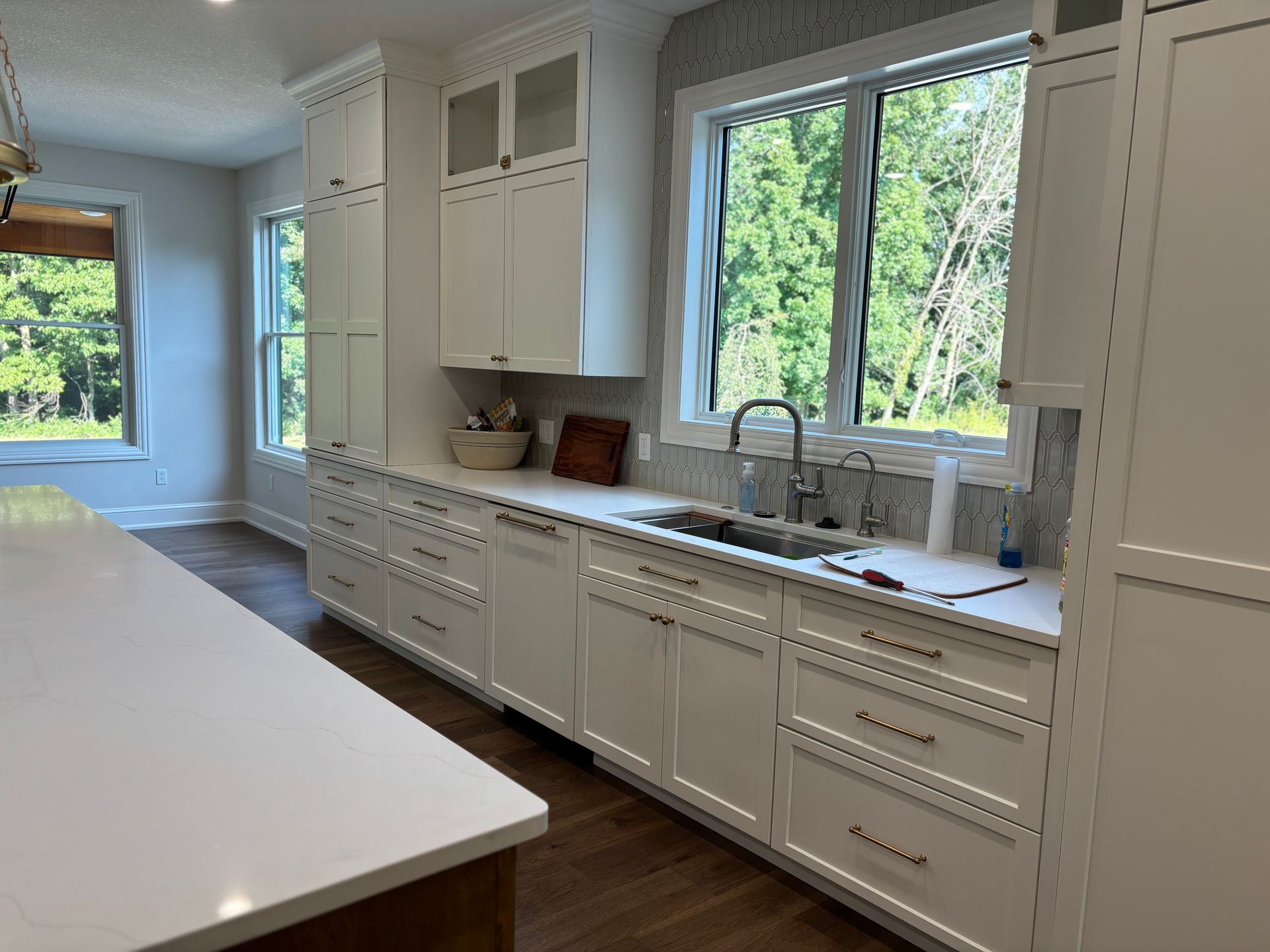 White kitchen with cabinets, countertops, and a window overlooking greenery.