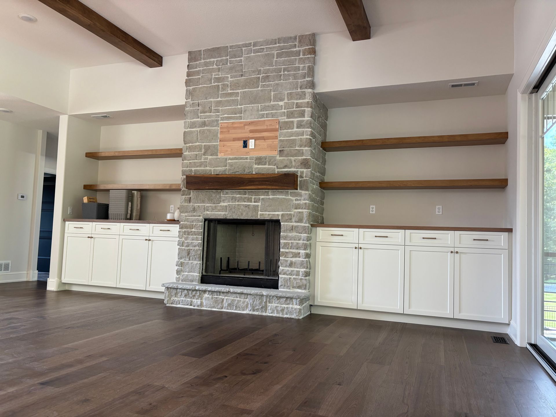 Living room with stone fireplace, built-in shelves, white cabinets, and wood beams.