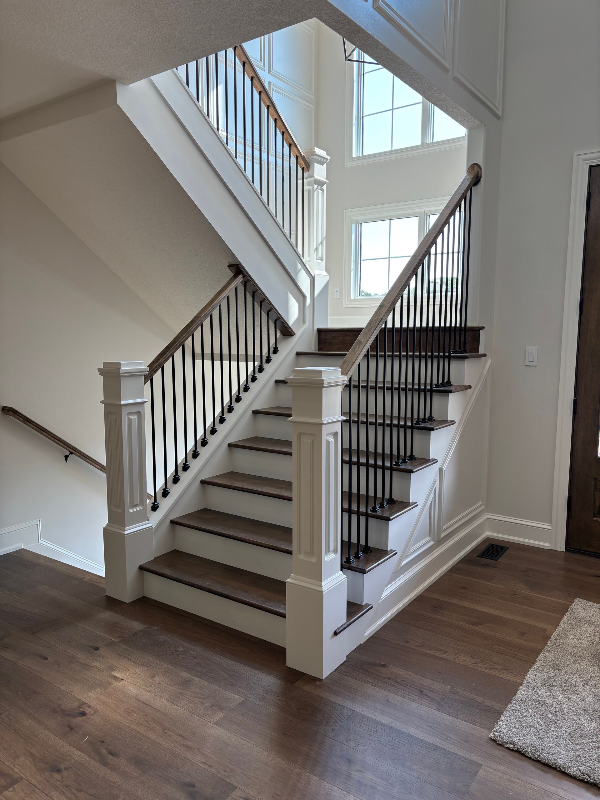 Two-story staircase with brown wood treads, white risers, black spindles, and a dark wood handrail.