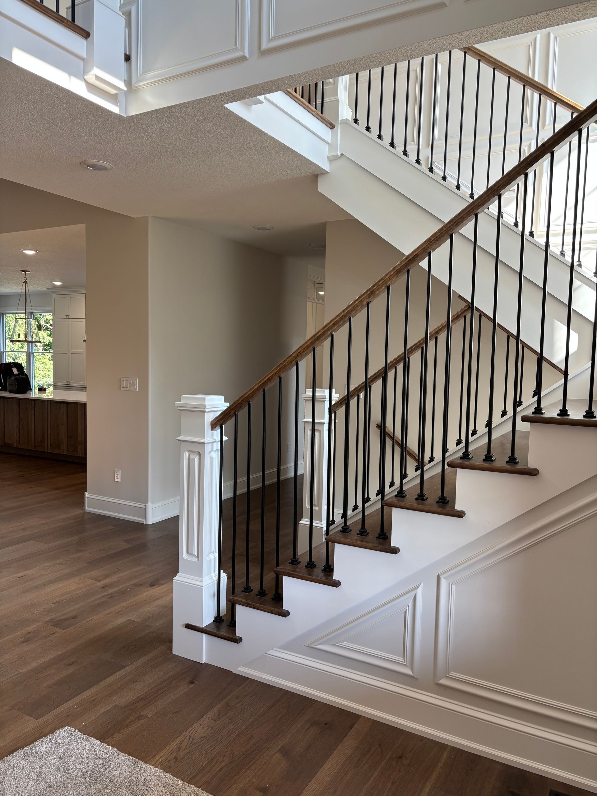 Wooden staircase with dark metal spindles and a light-colored railing, in a modern home.