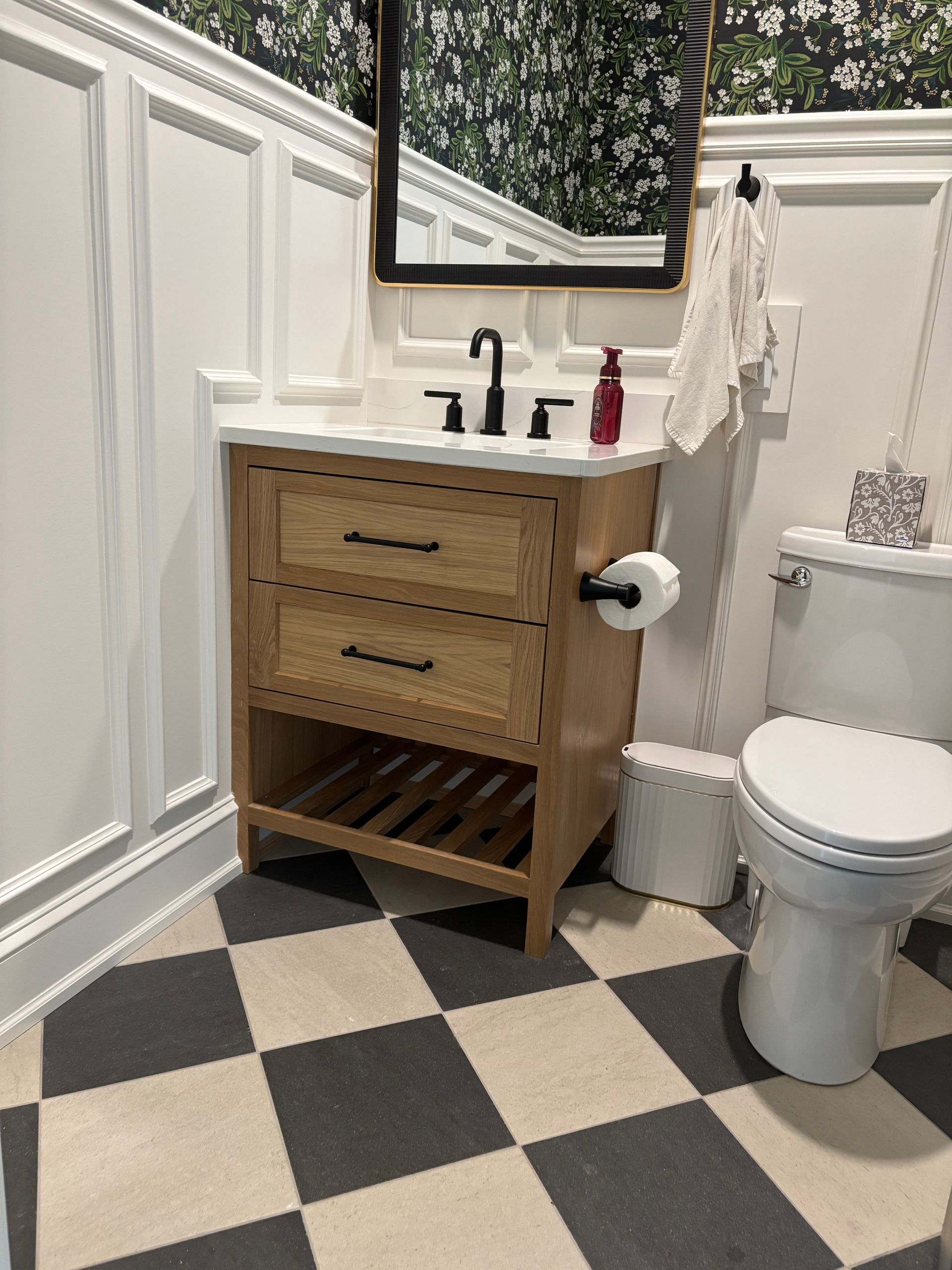 Bathroom with wooden vanity, black faucet, checkered floor, and floral wallpaper.