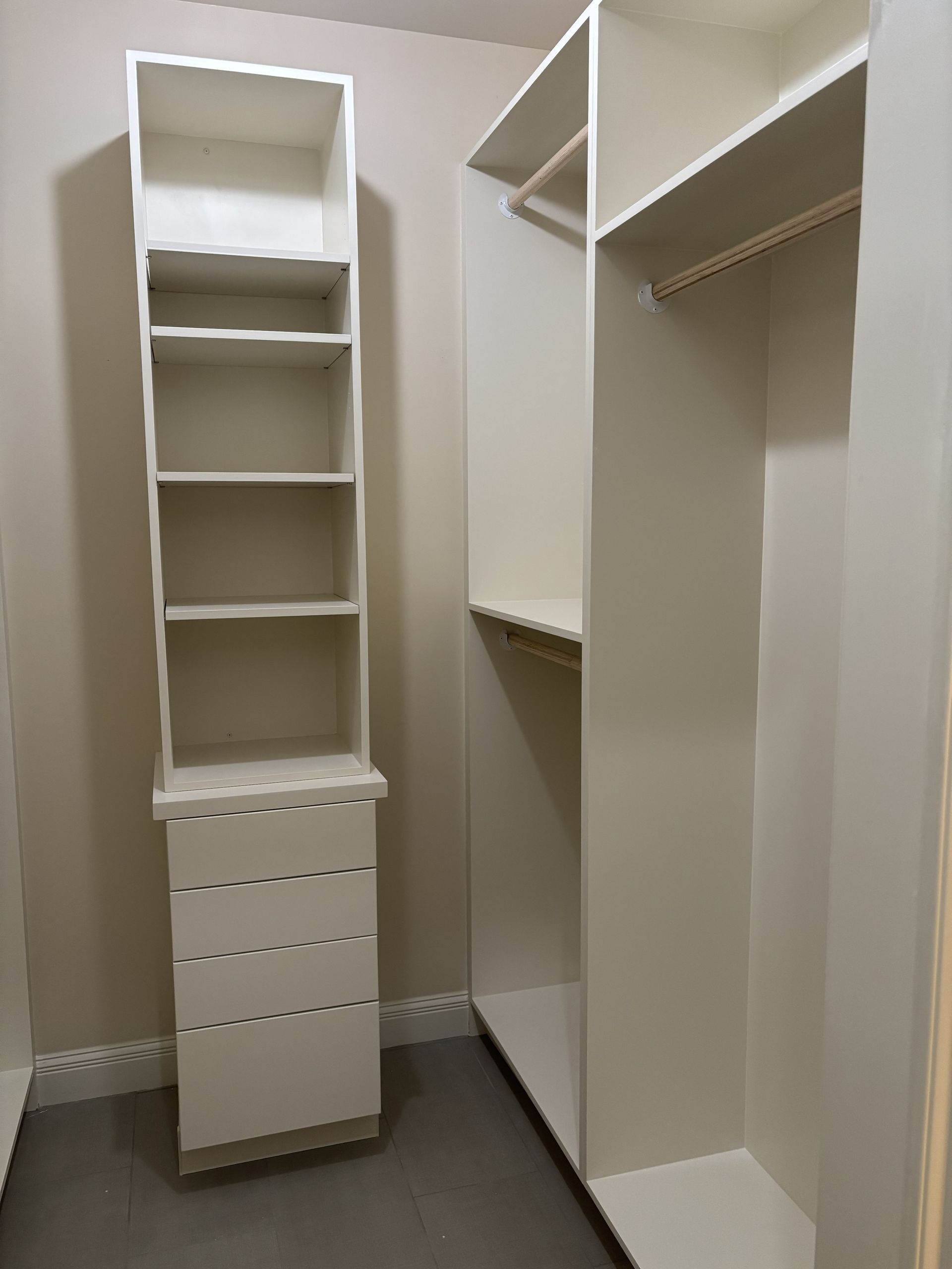White closet shelving unit with drawers and hanging rod in a room with beige walls and gray carpet.