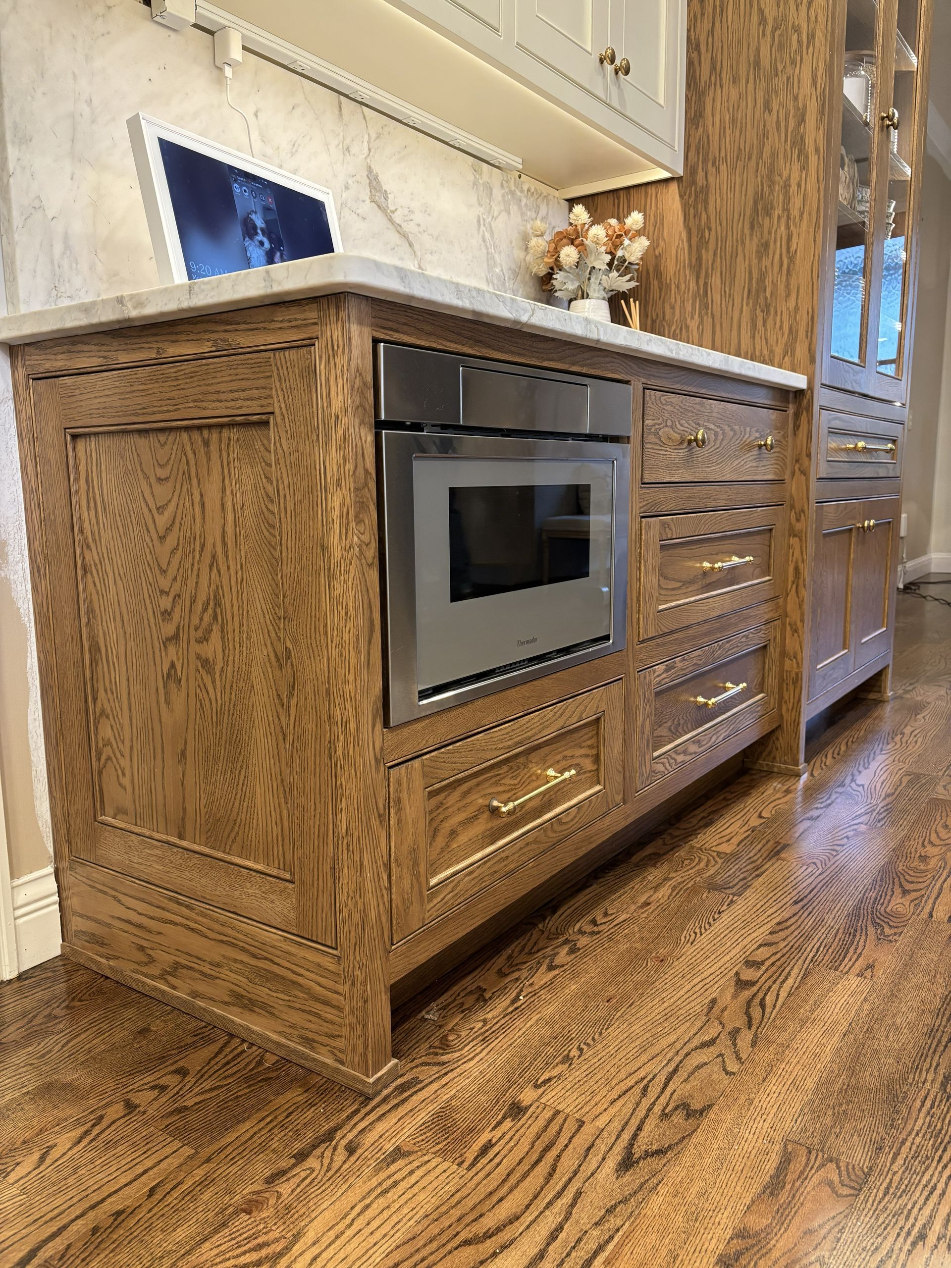 Wooden kitchen island with built-in microwave, drawers, and marble countertop, set on hardwood floor.