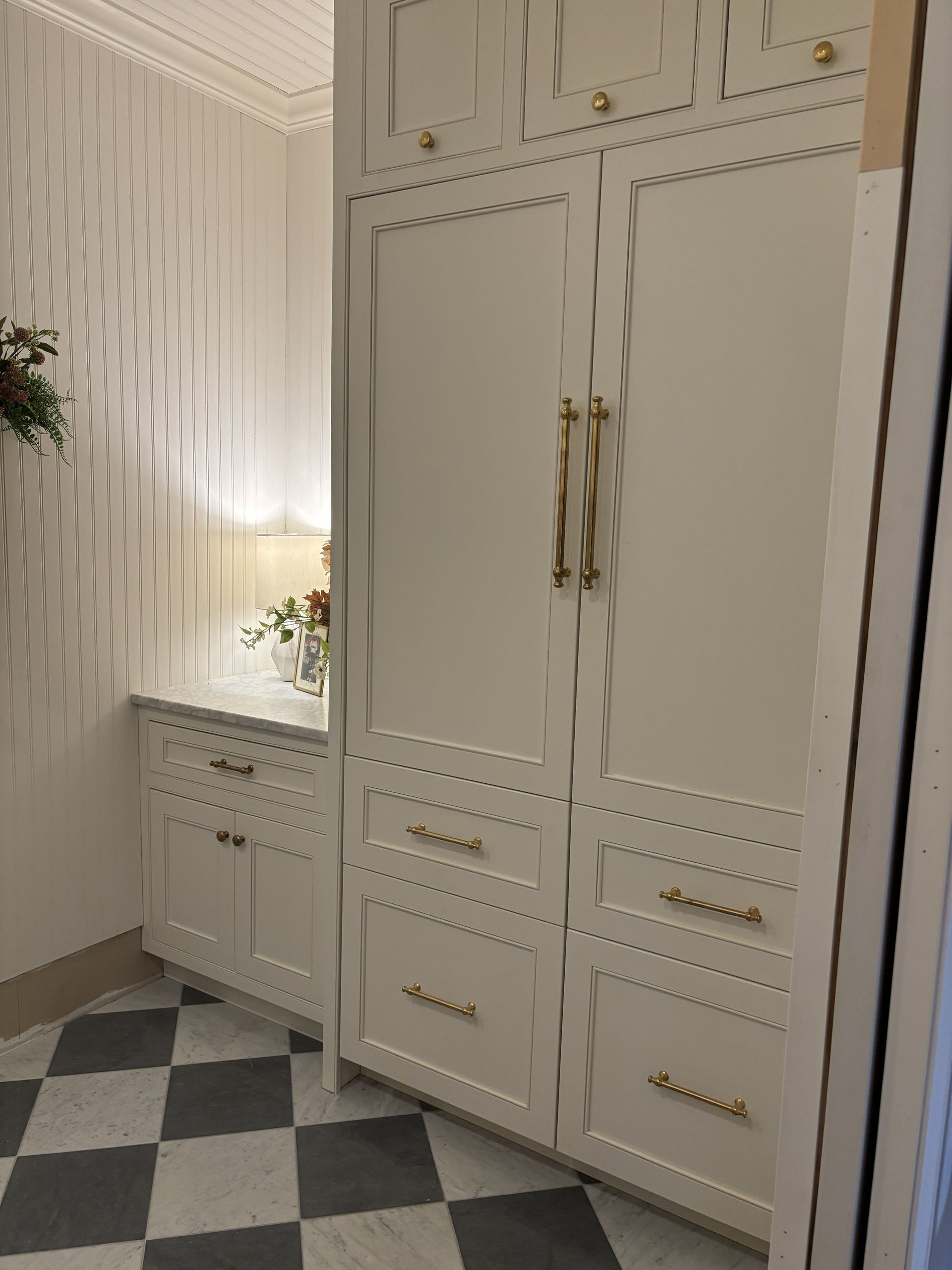White built-in cabinets with gold hardware in a room with black and white checkered floor.