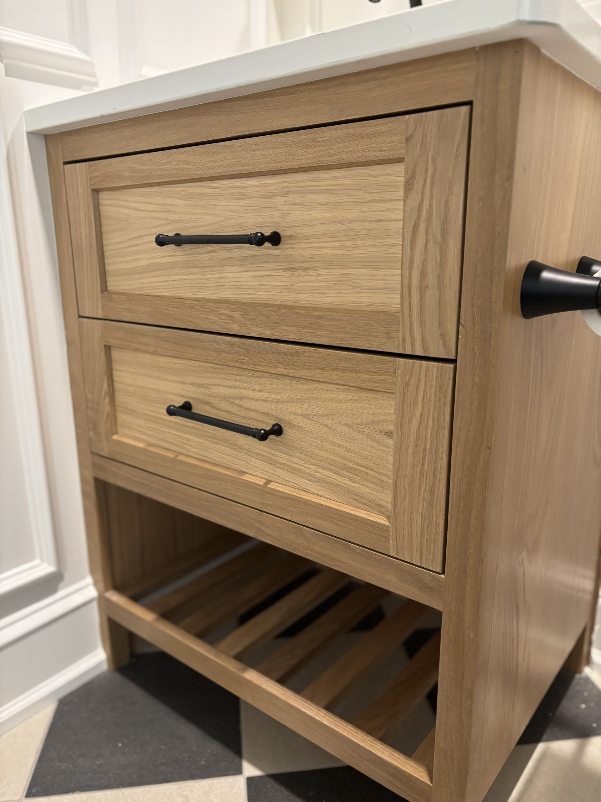 Bathroom vanity with two drawers and an open shelf, light wood finish, black hardware.