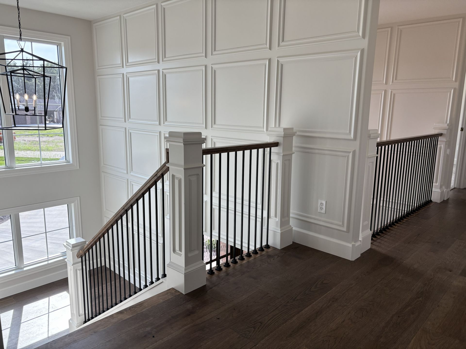Interior view of a staircase with white paneling and dark wood floors and railings.