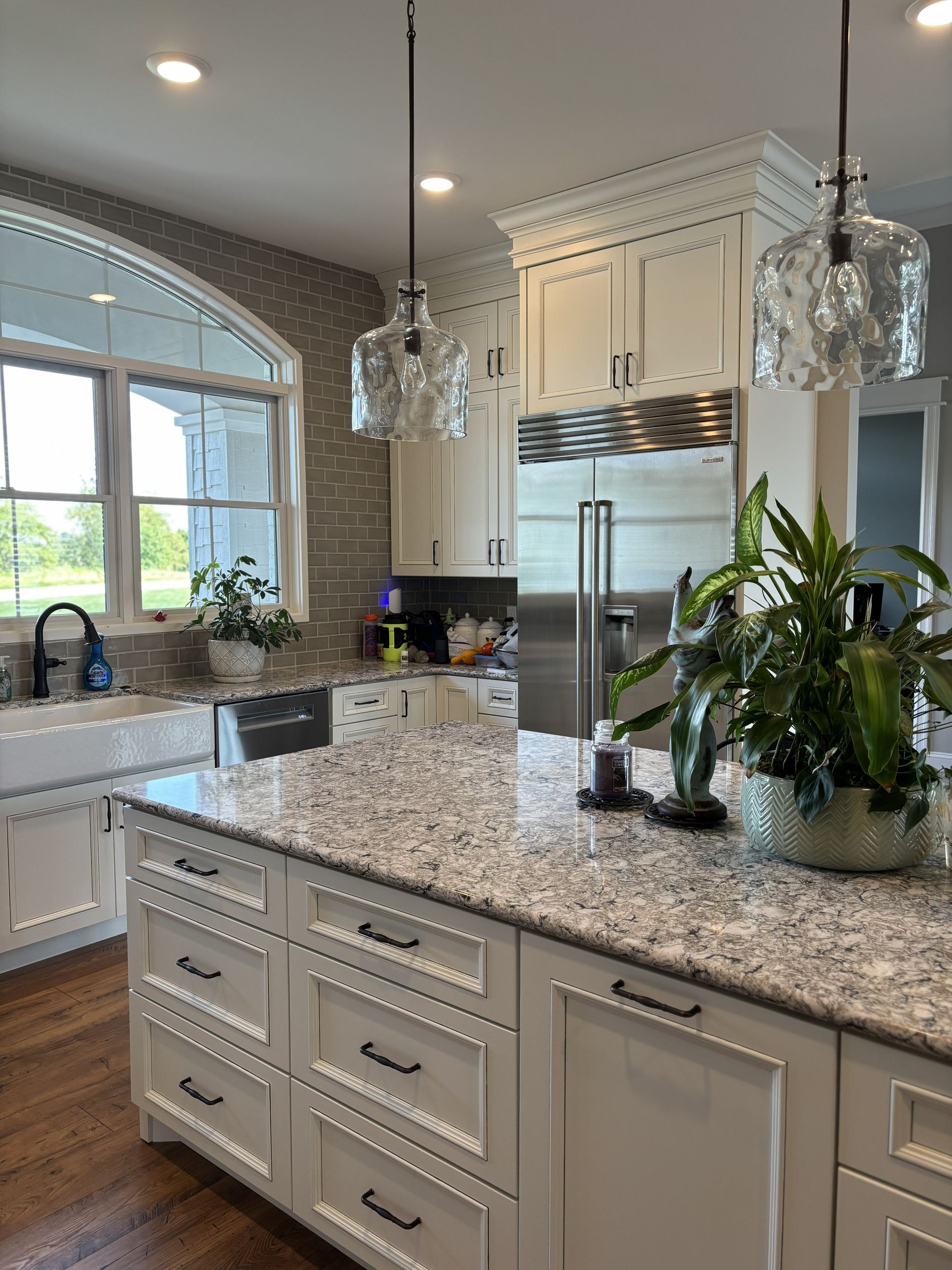 Spacious white kitchen with a large island, granite countertop, and glass pendant lights.